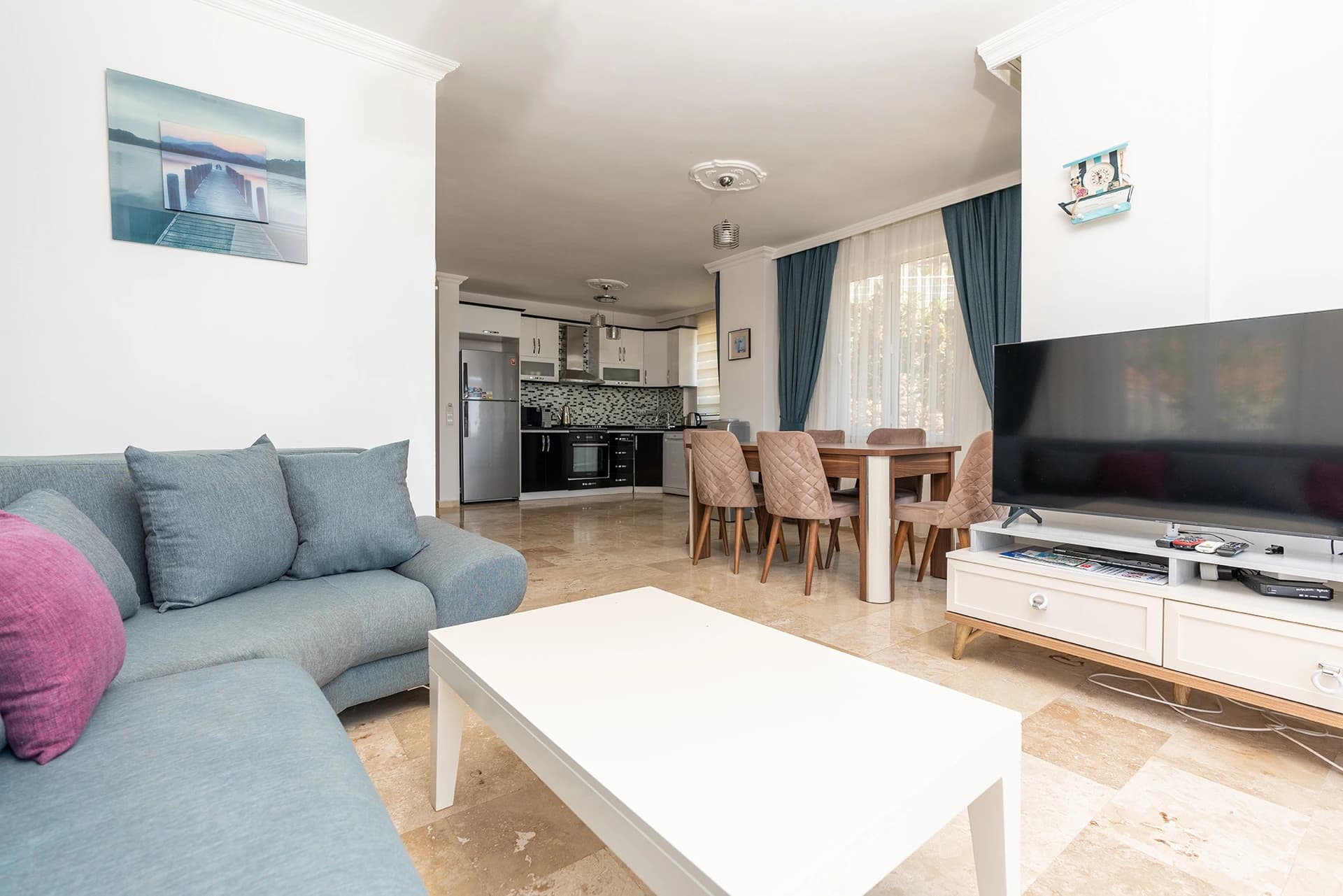 Open-plan living and dining area with integrated kitchen, modern furnishings, and entertainment system.