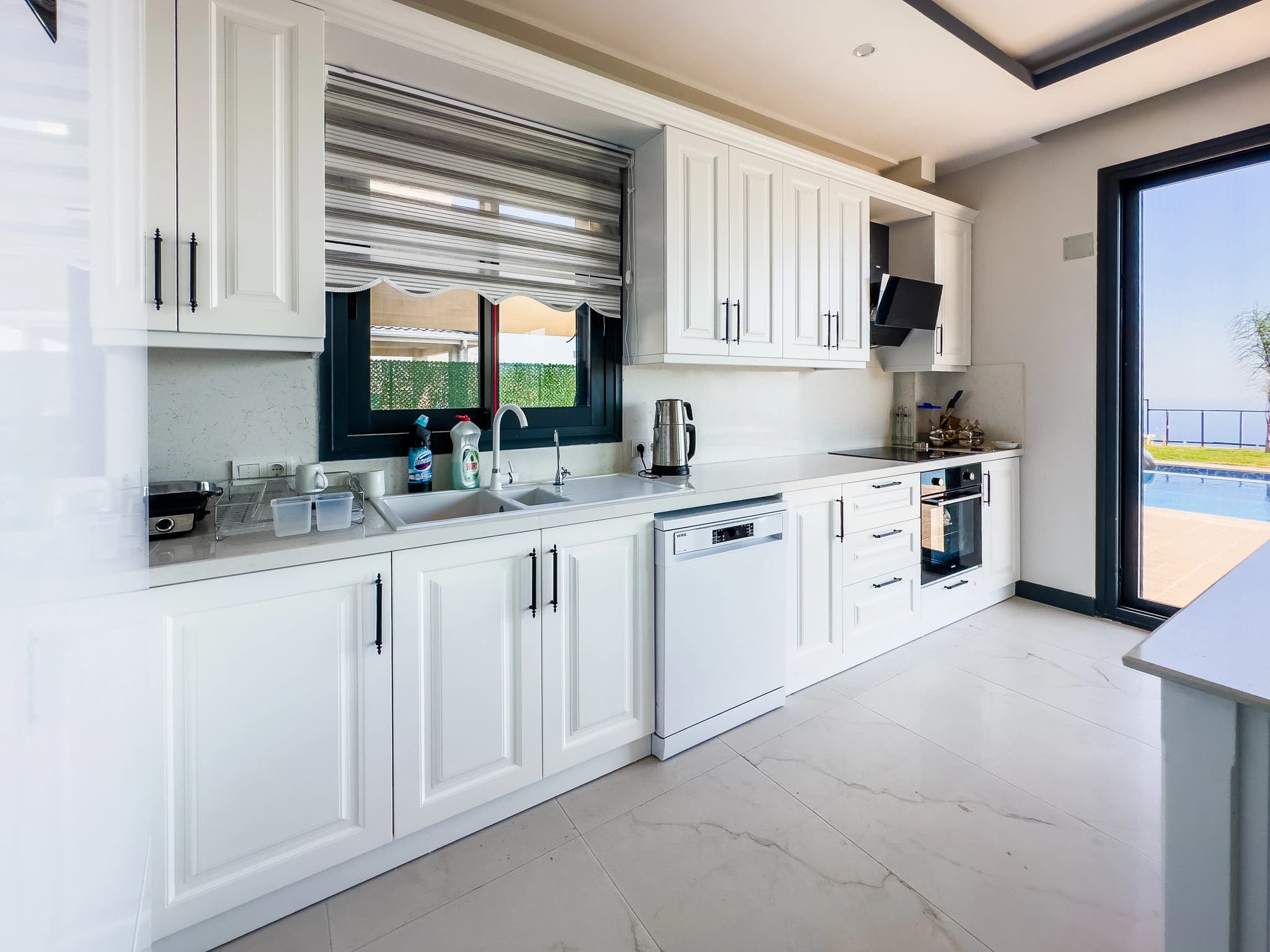 Modern white kitchen with stainless steel appliances, abundant storage, and pool-side access.