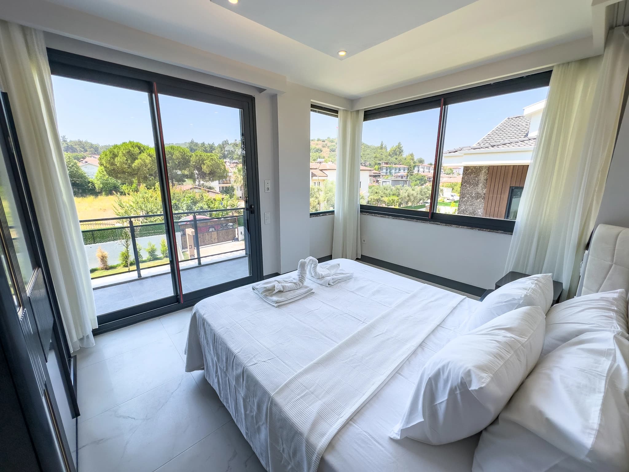 Bright master bedroom with king bed, floor-to-ceiling windows, and expansive mountain views from private balcony.