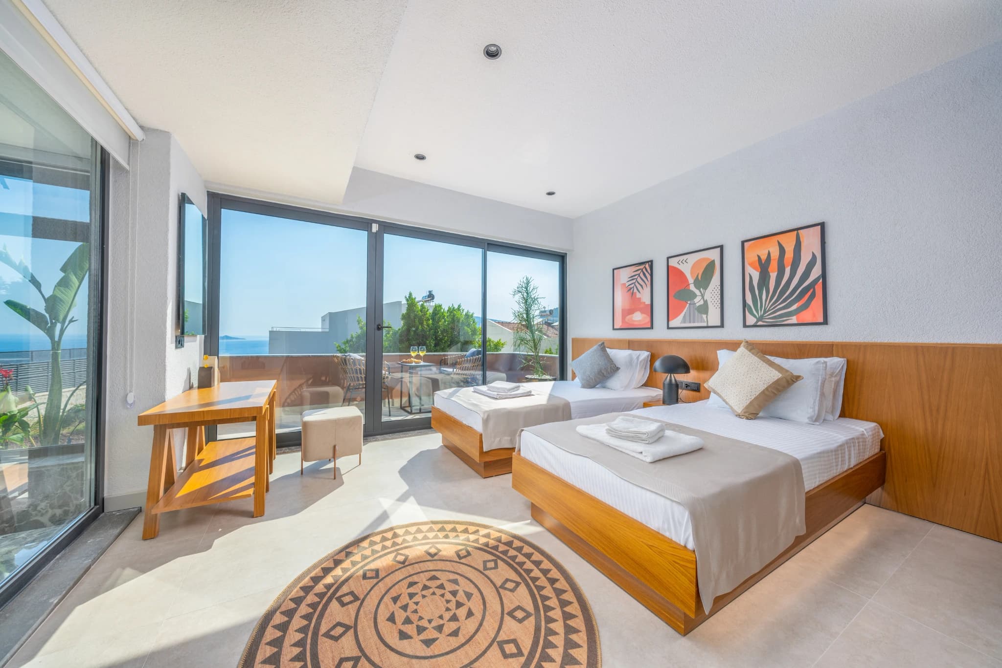 Bright bedroom with twin queen beds, sea-view terrace, and work desk.