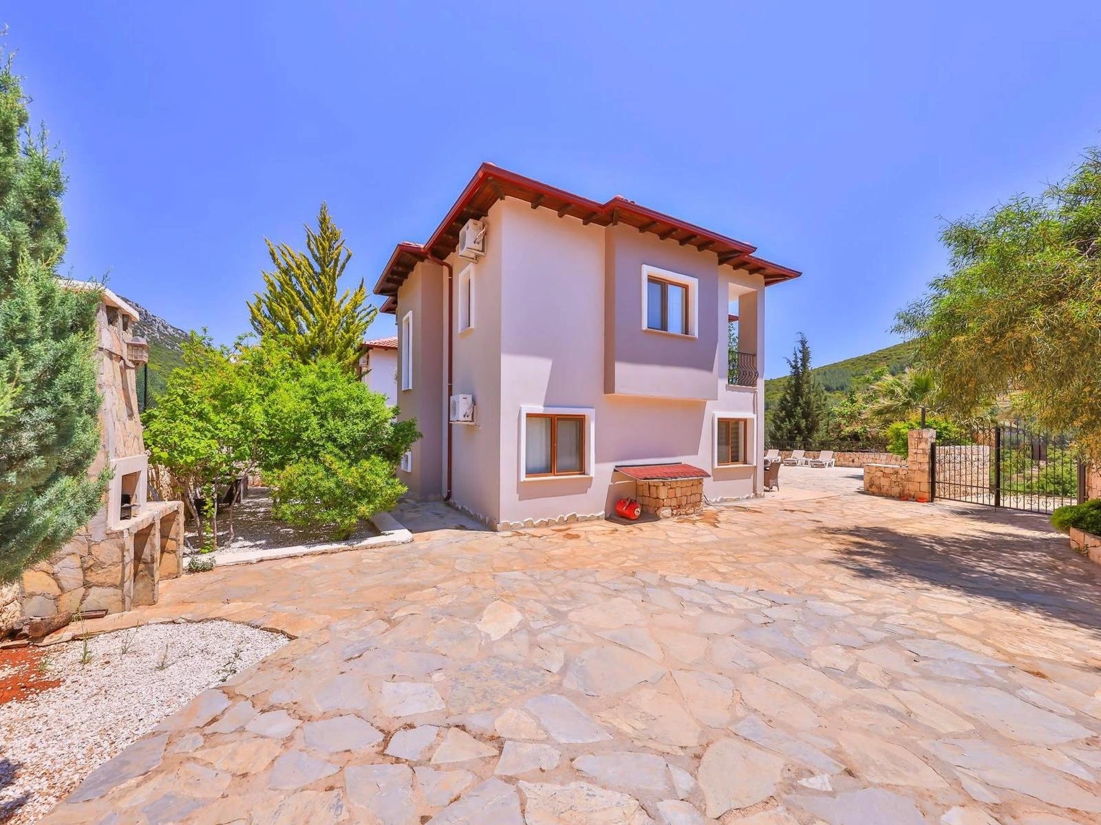 Front exterior of the pink villa with stone courtyard and surrounding gardens.