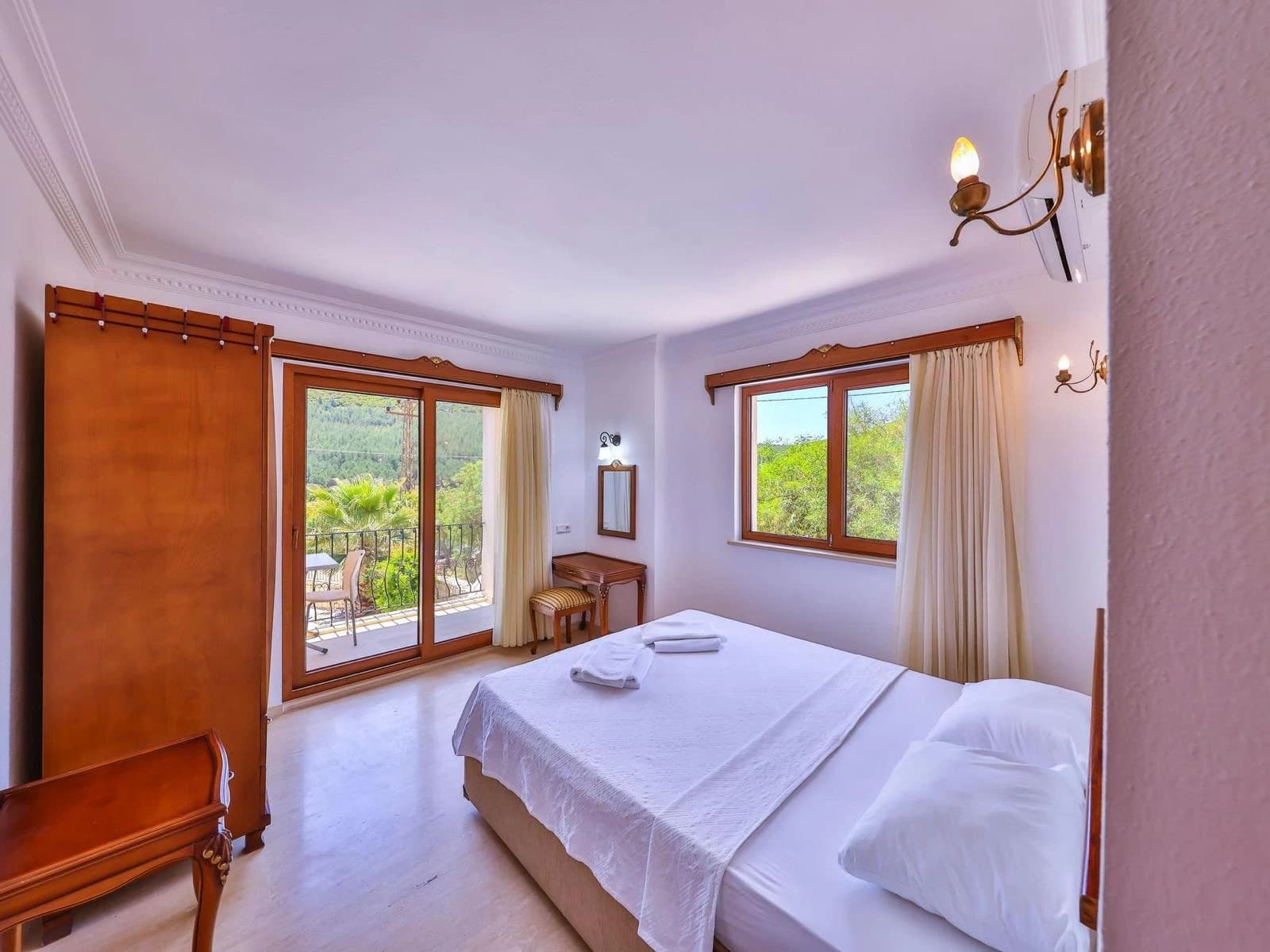 Bright bedroom with double bed, balcony access, and panoramic garden and mountain views.