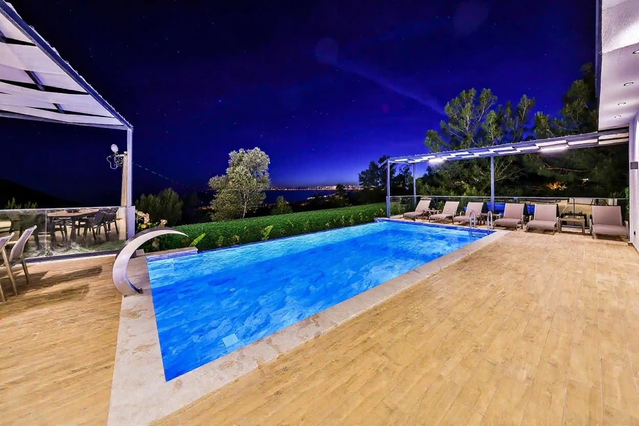 Beautifully lit pool at night with multiple loungers and panoramic views.