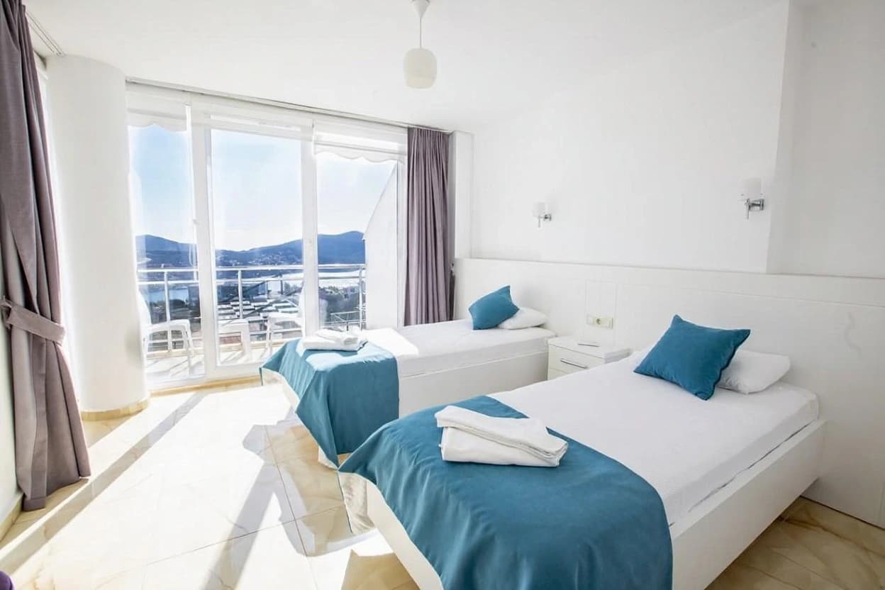 Twin bedroom with stunning sea and mountain views through floor-to-ceiling glass doors.