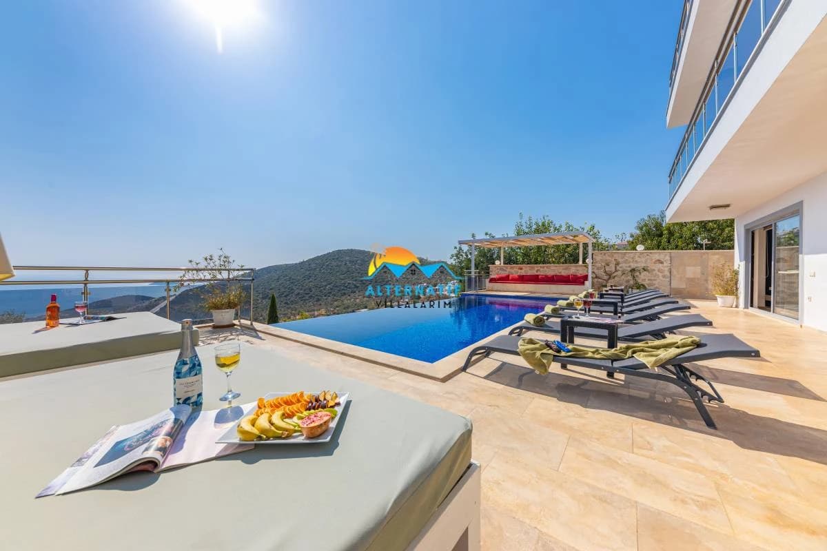 Luxurious pool terrace with infinity-edge private pool, multiple sun loungers, mountain and sea vistas, and refreshments.