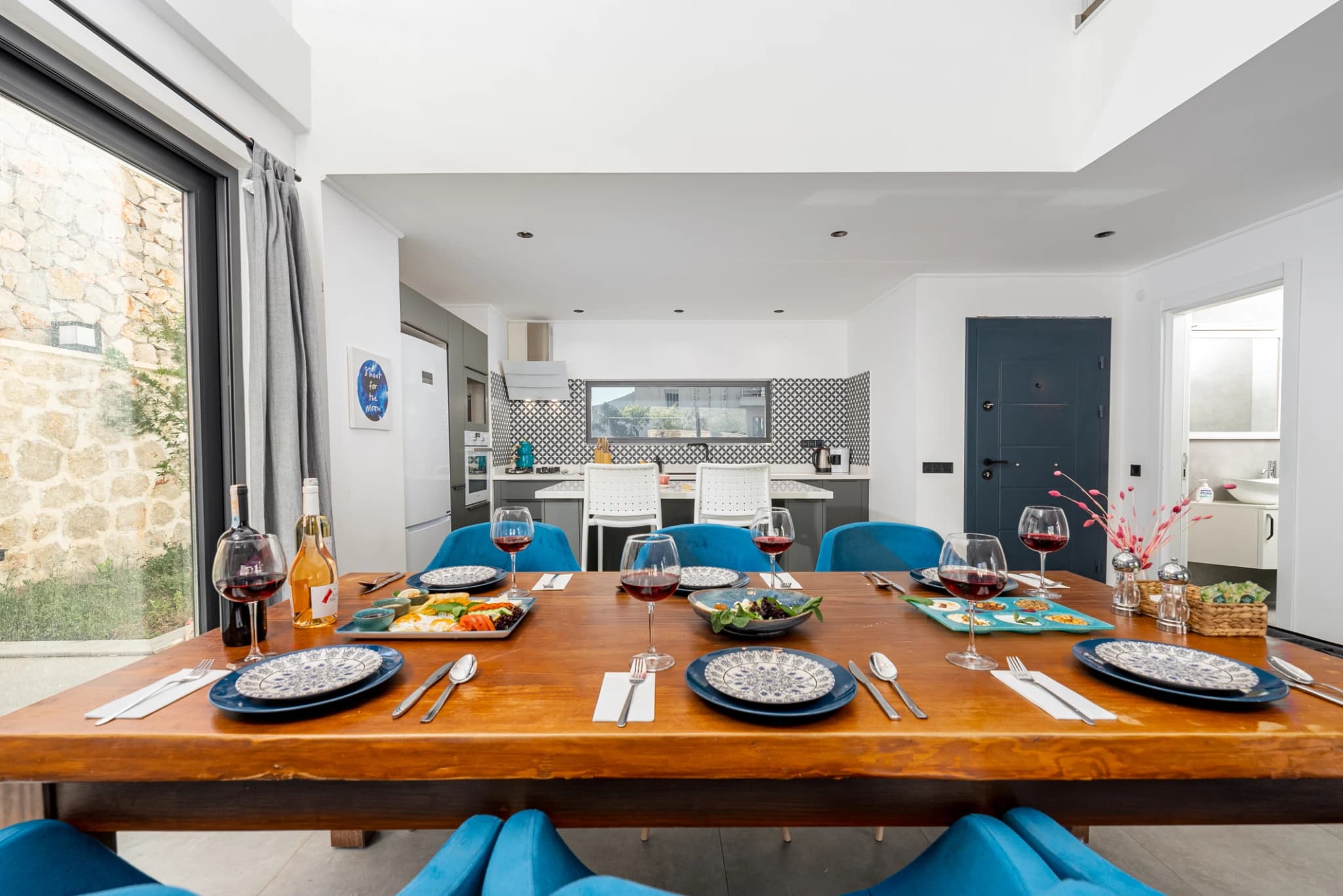 Stylish dining area with wooden table, blue seating, kitchen view, and garden access.