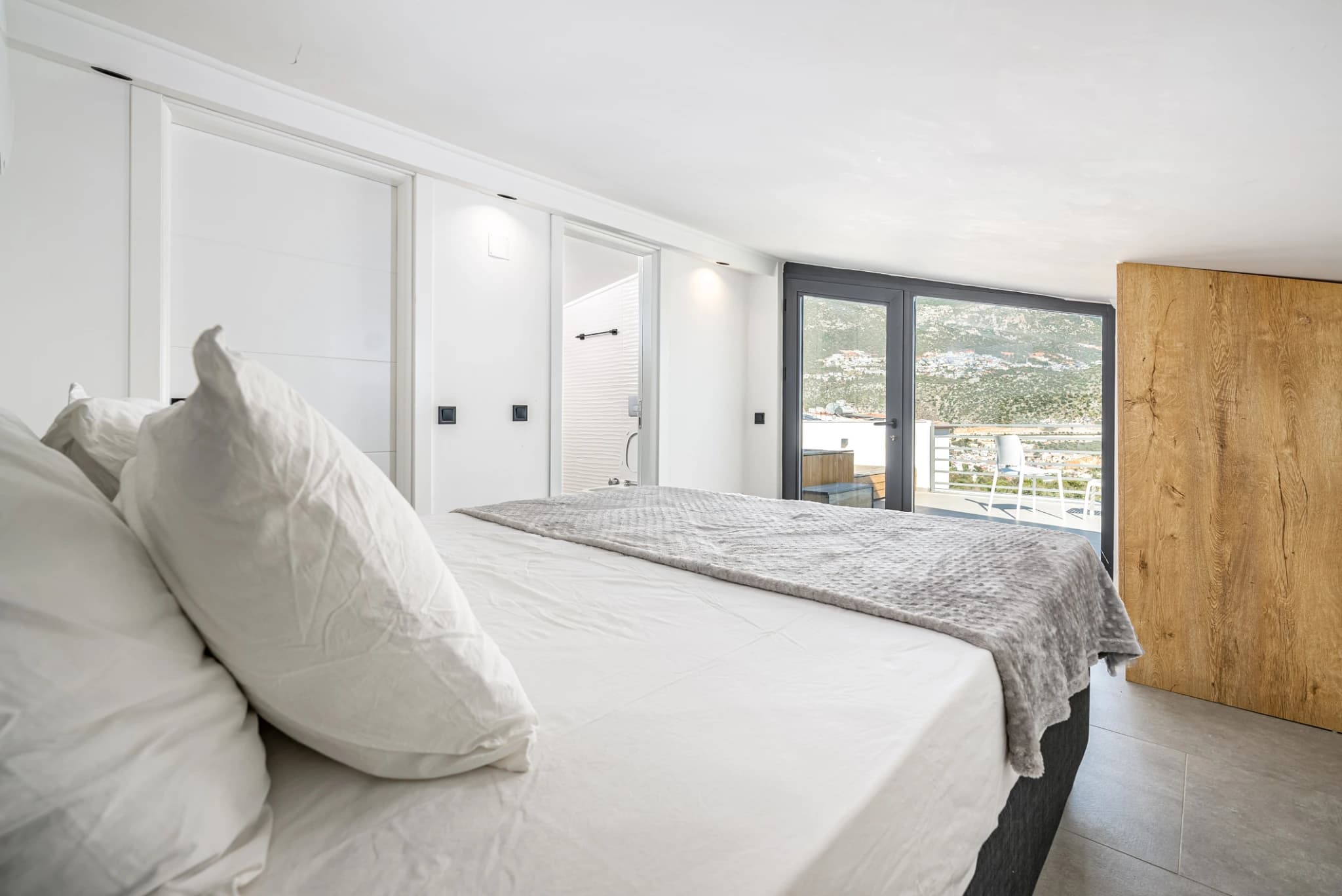 Modern bedroom featuring king bed with terrace access overlooking hillside landscape.