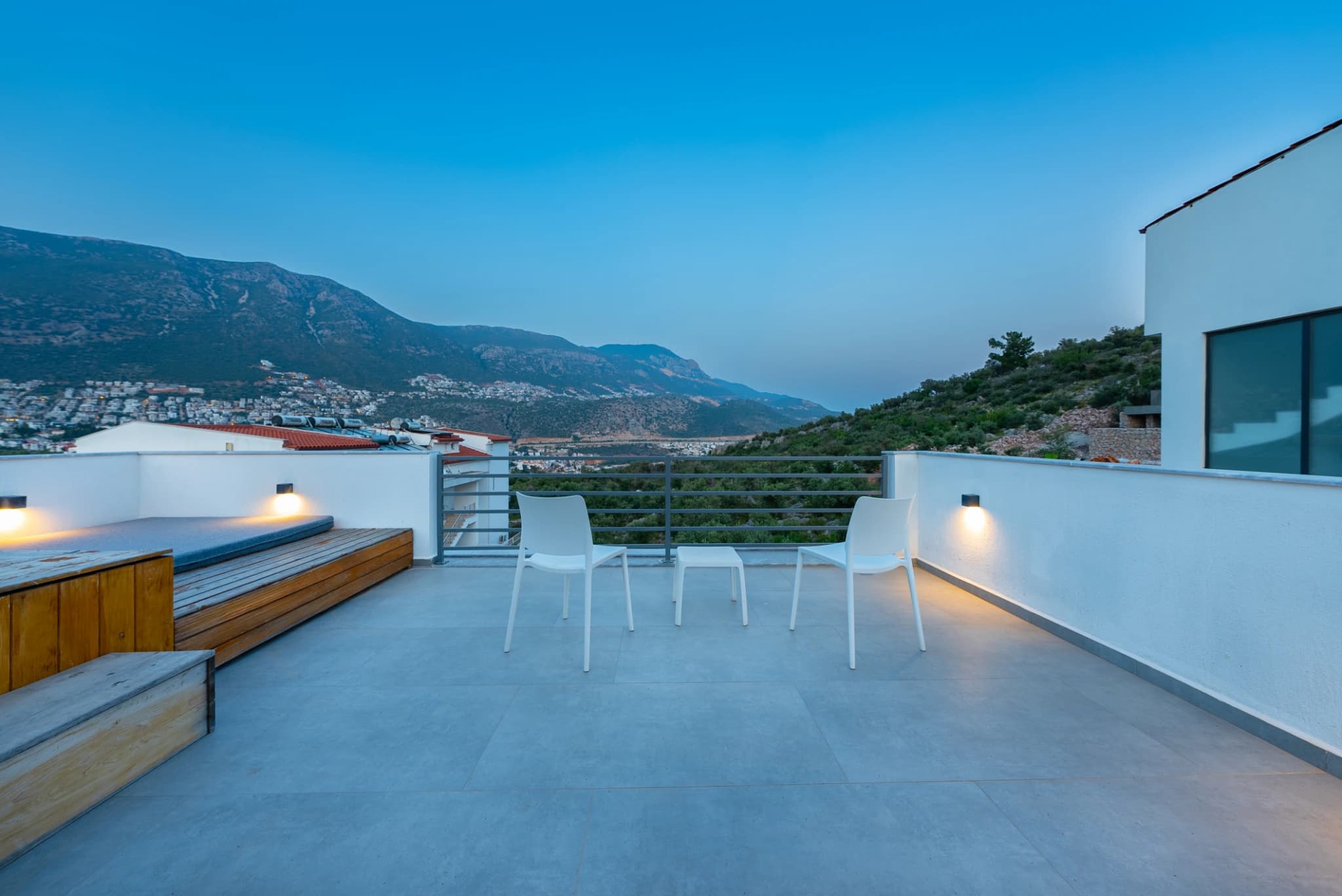 Elevated terrace overlooking mountains and coastline with spa tub and modern outdoor furniture.