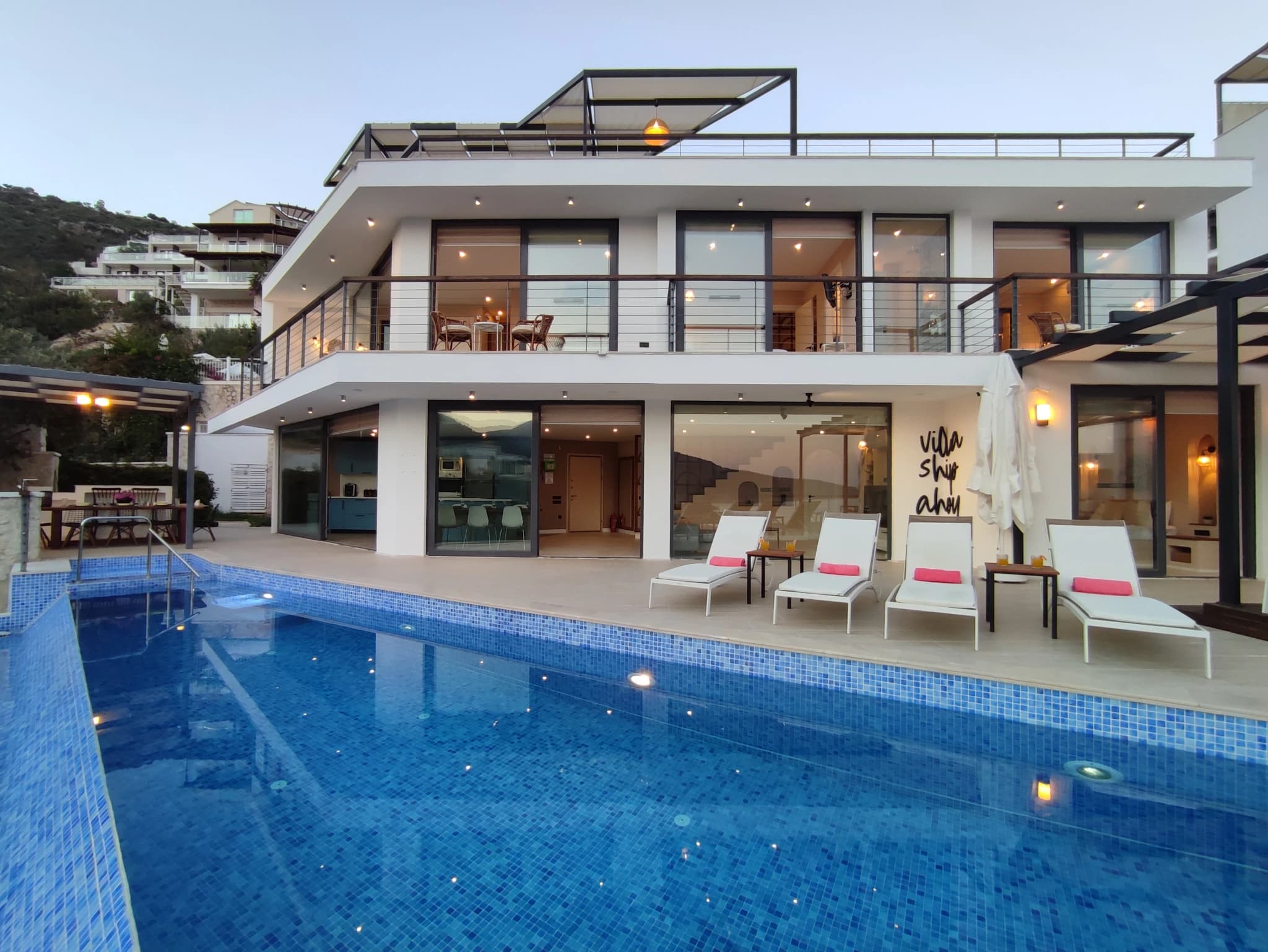Stunning private pool with sun loungers overlooking the modern villa at dusk.