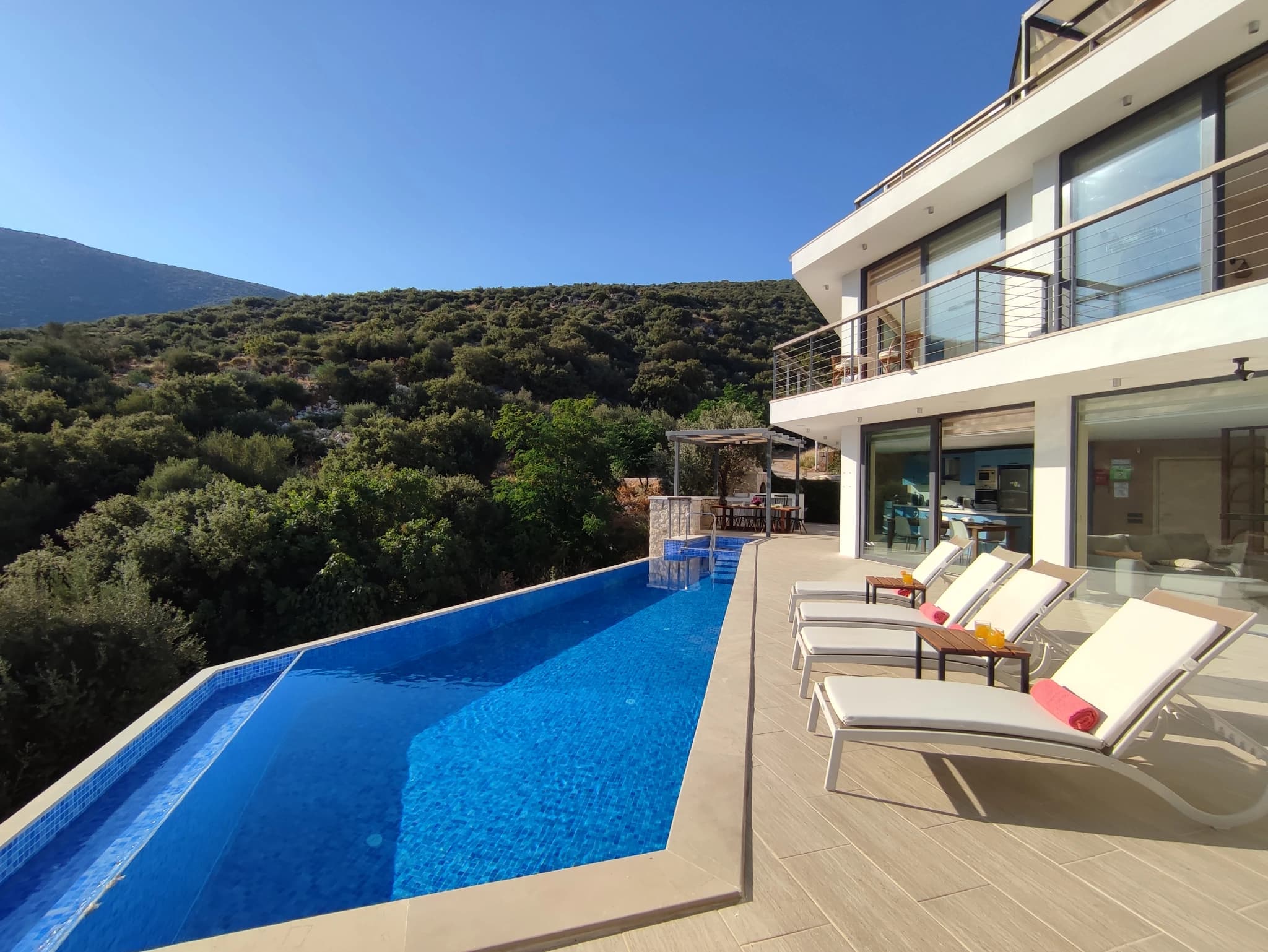 Stunning infinity pool with sun loungers overlooking mountains and sea.