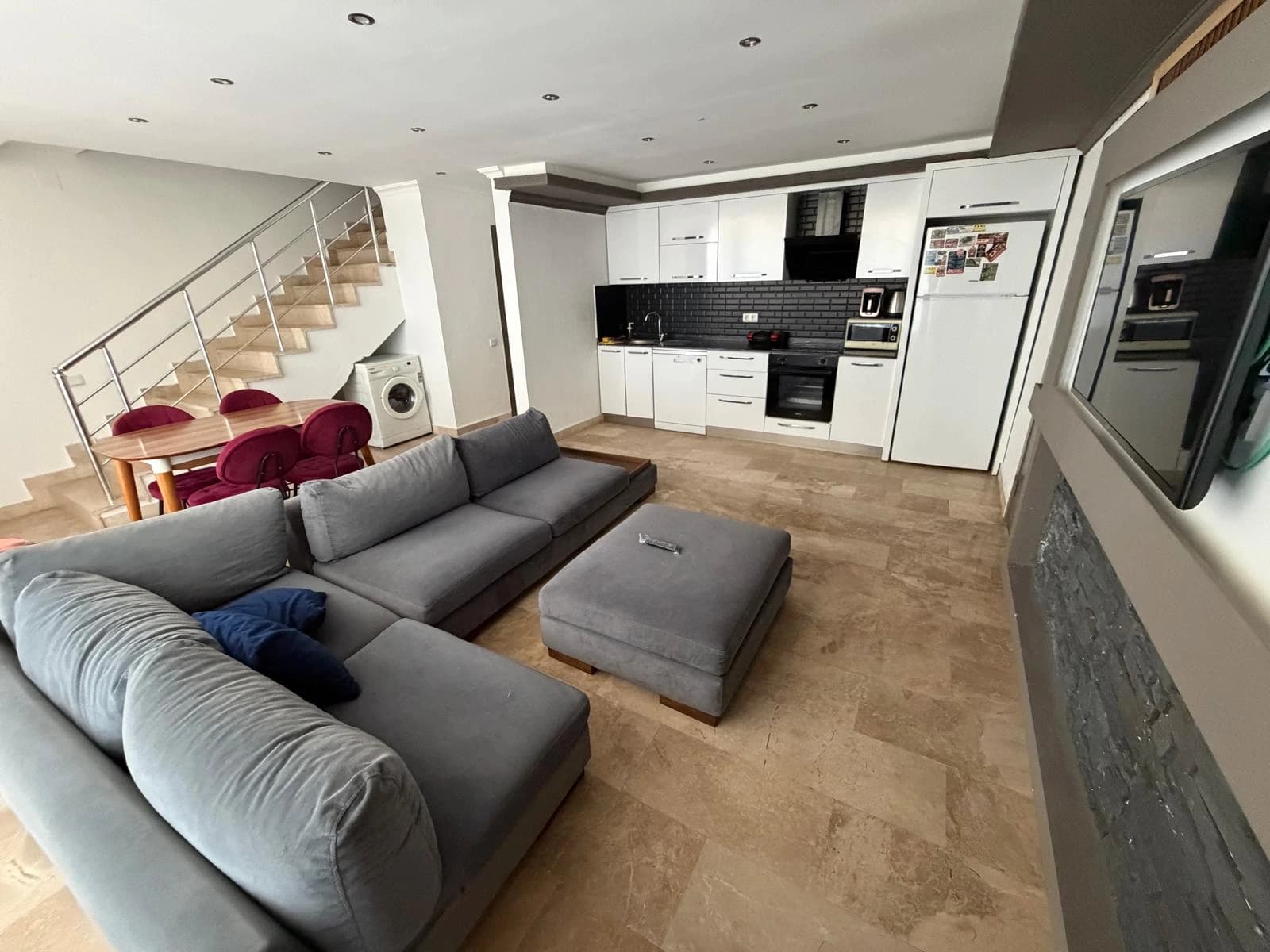Open-plan living room with large gray sofa and integrated kitchen area.