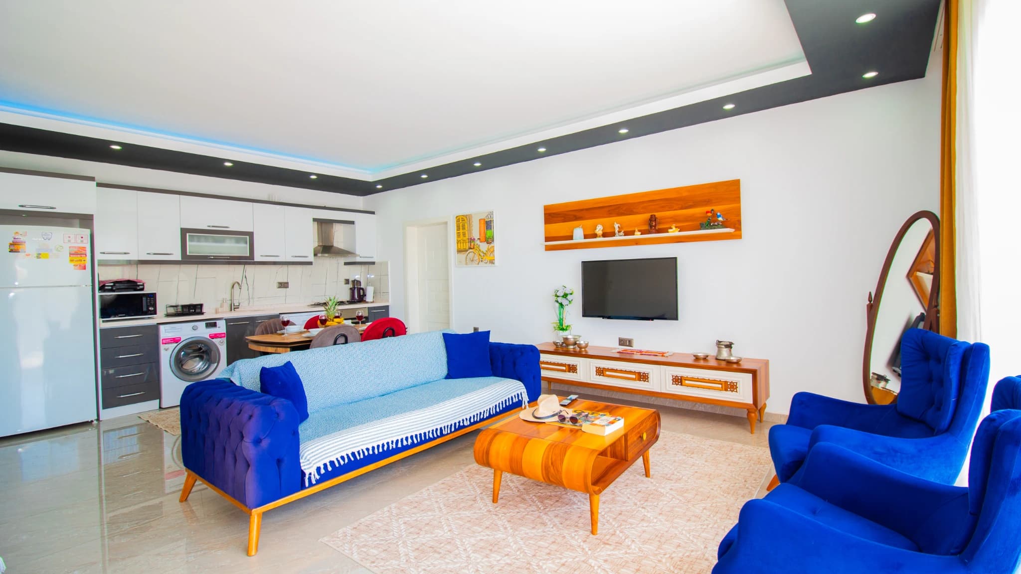 Contemporary living room with bold blue sofas and orange accents overlooking kitchen.