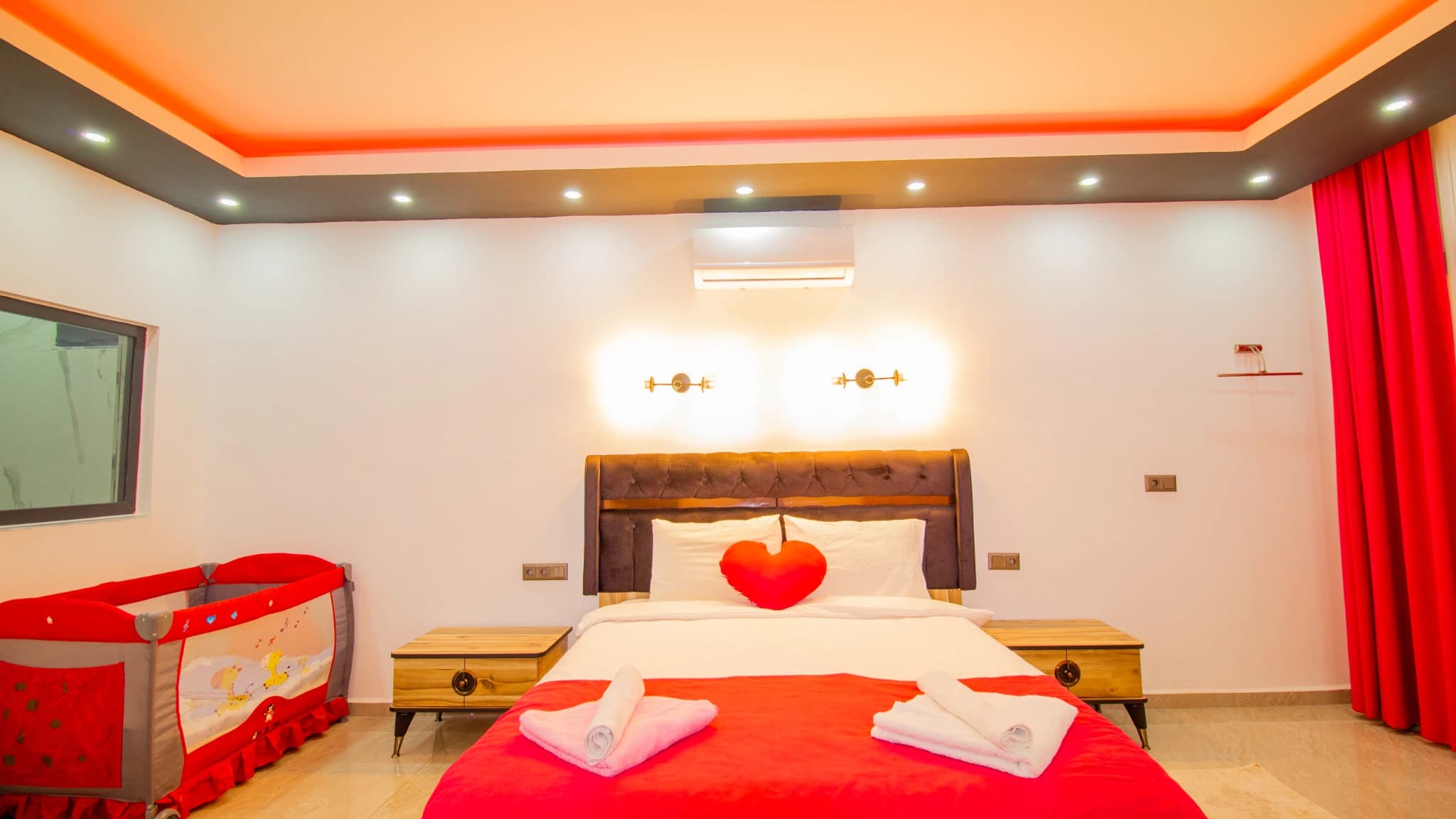 Modern bedroom with queen bed, decorative red heart pillow, and dramatic ceiling lighting.
