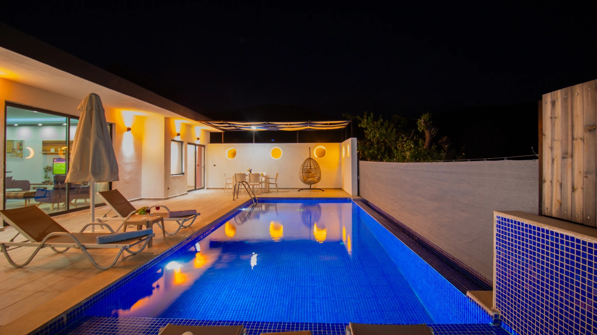 Blue-tiled pool with lounge chairs and decorative lighting.