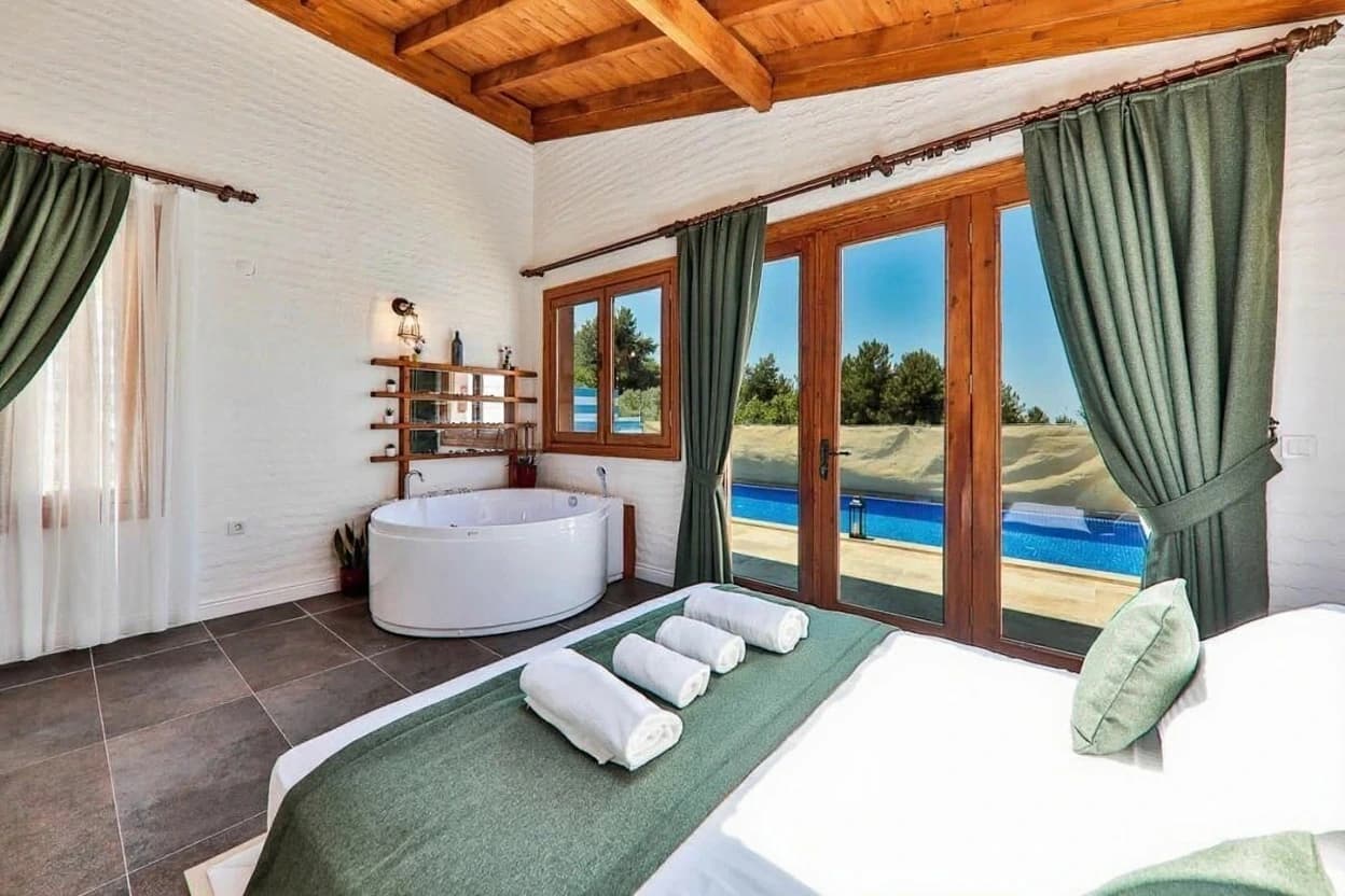 Kaş İslamlar'da Özel Havuzlu, Jakuzili ve Deniz Manzaralı 2 Yatak Odalı Korunaklı Villa – Spacious bedroom suite with king bed, freestanding bathtub, pool view, and glass doors to terrace.