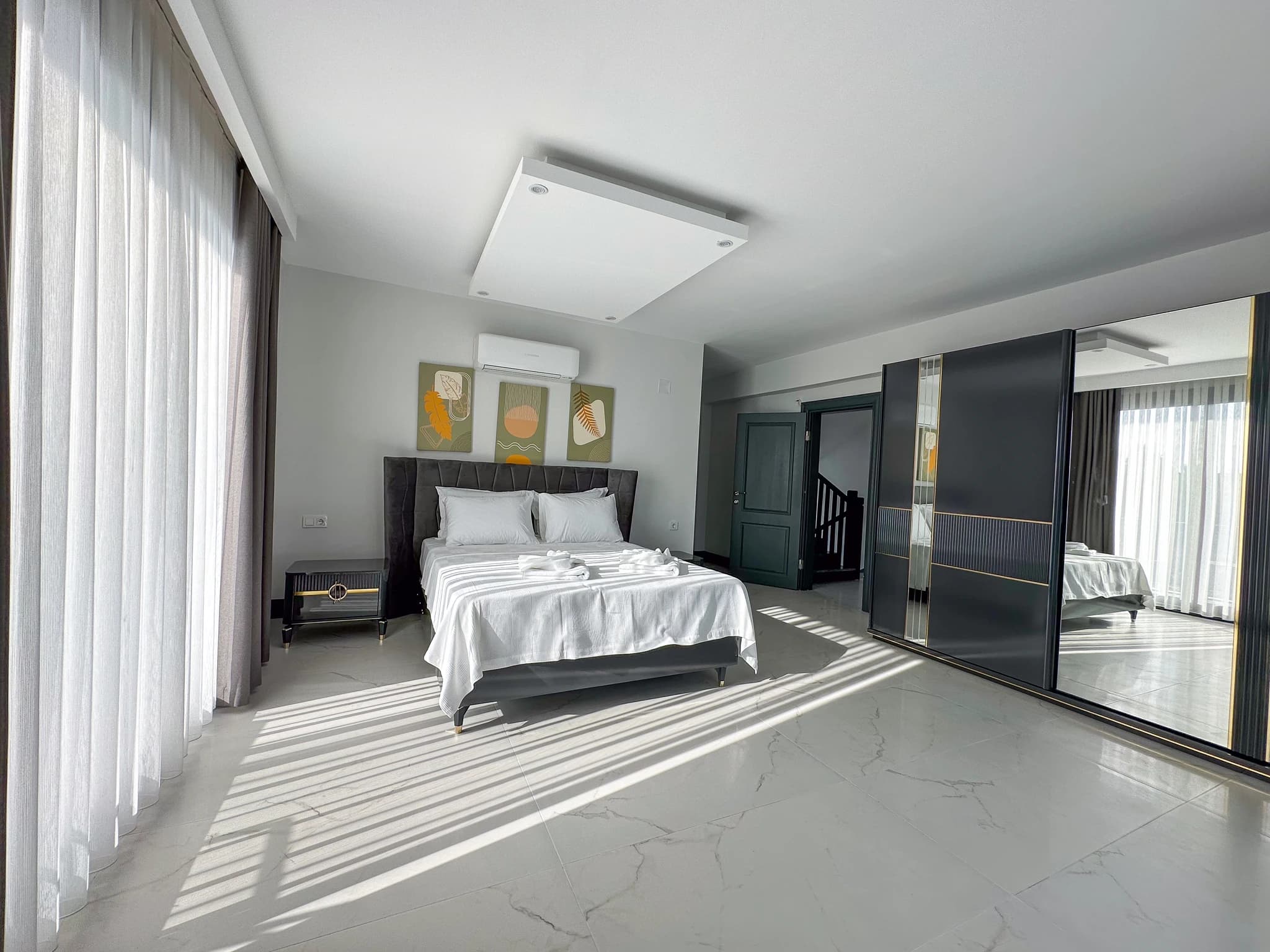 Bright bedroom with queen bed, large balcony windows, and contemporary dark furnishings.