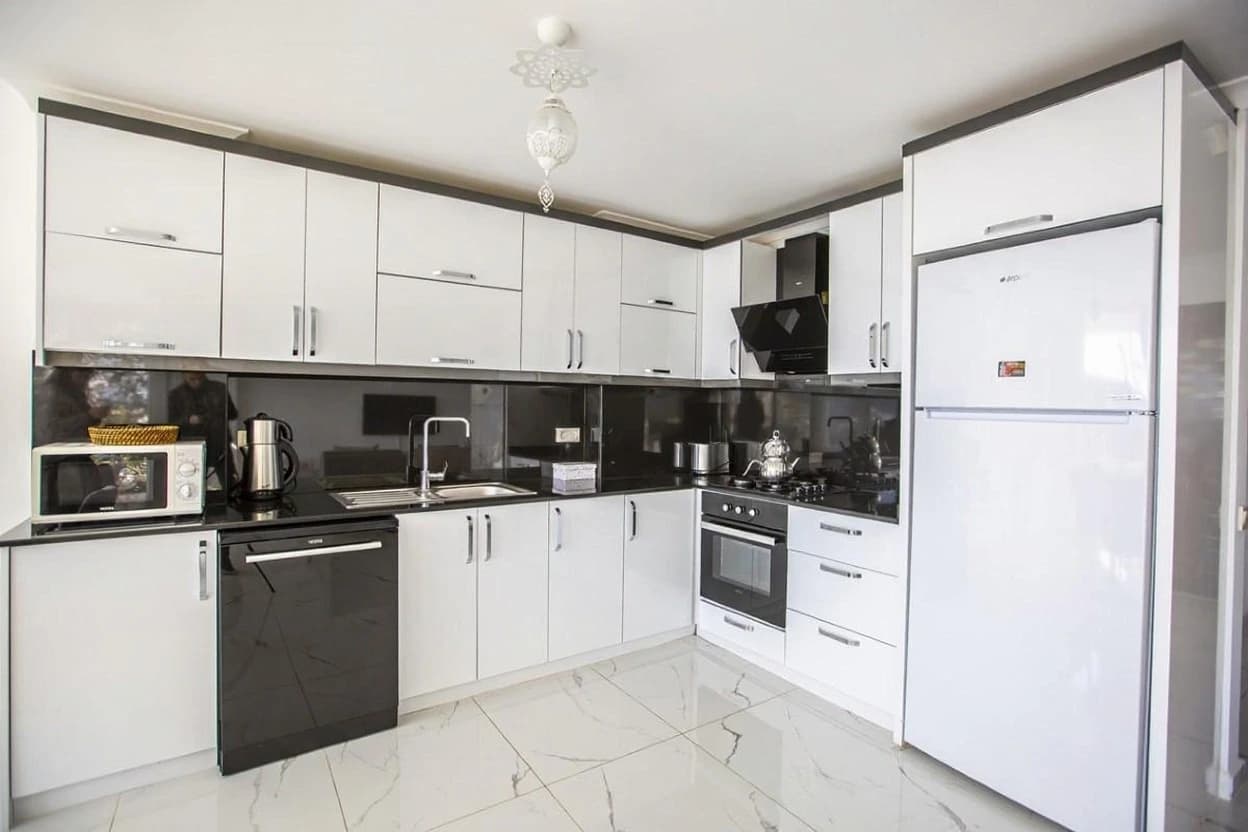 Modern U-shaped kitchen with white cabinetry, black granite backsplash, and stainless steel appliances.