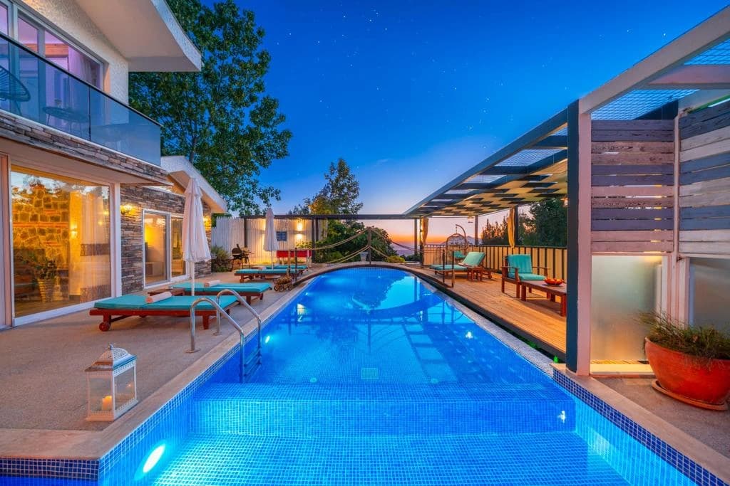 Illuminated private pool at dusk with loungers and mountain views.