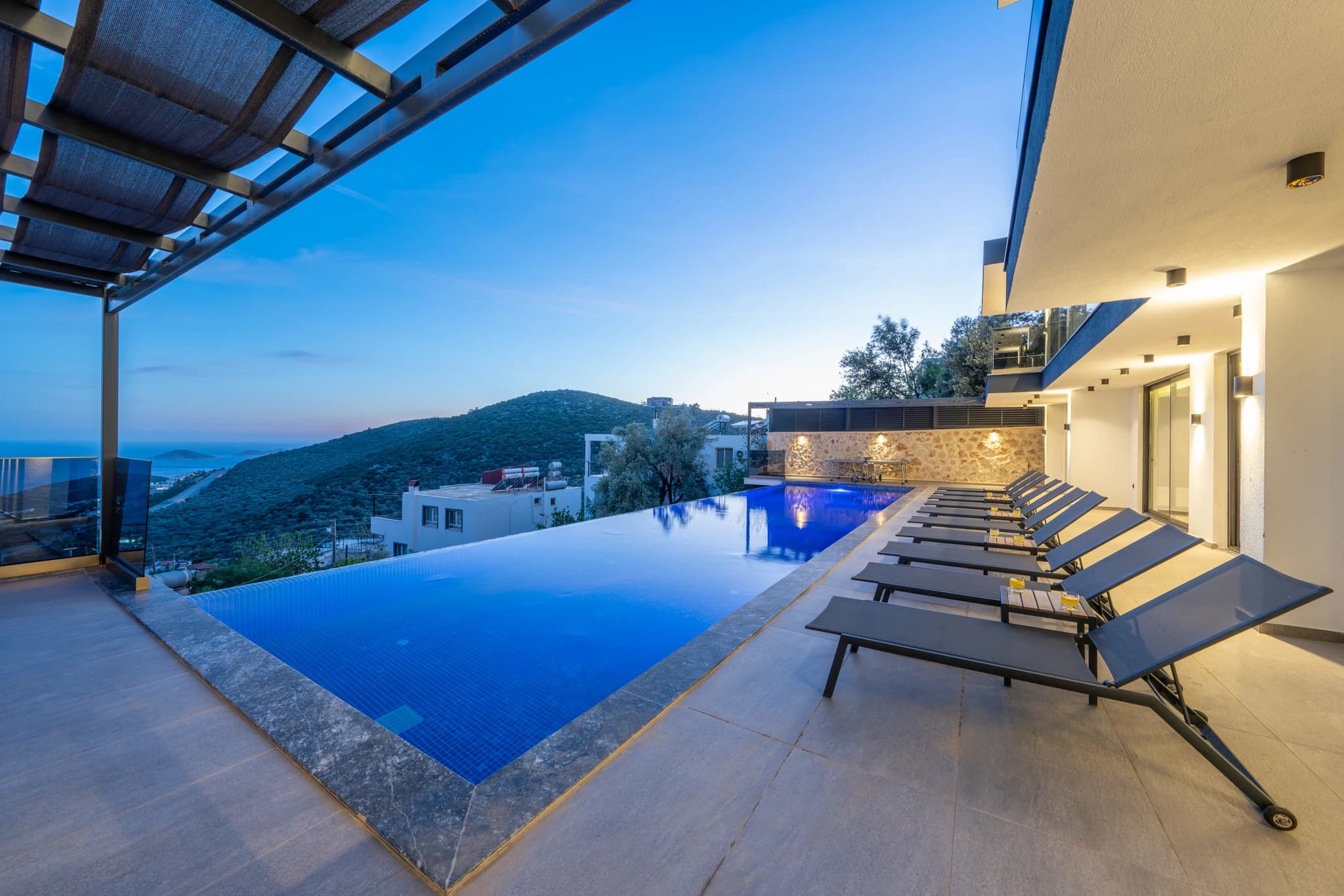 Stunning private pool with illuminated loungers overlooking the Mediterranean coastline at dusk.