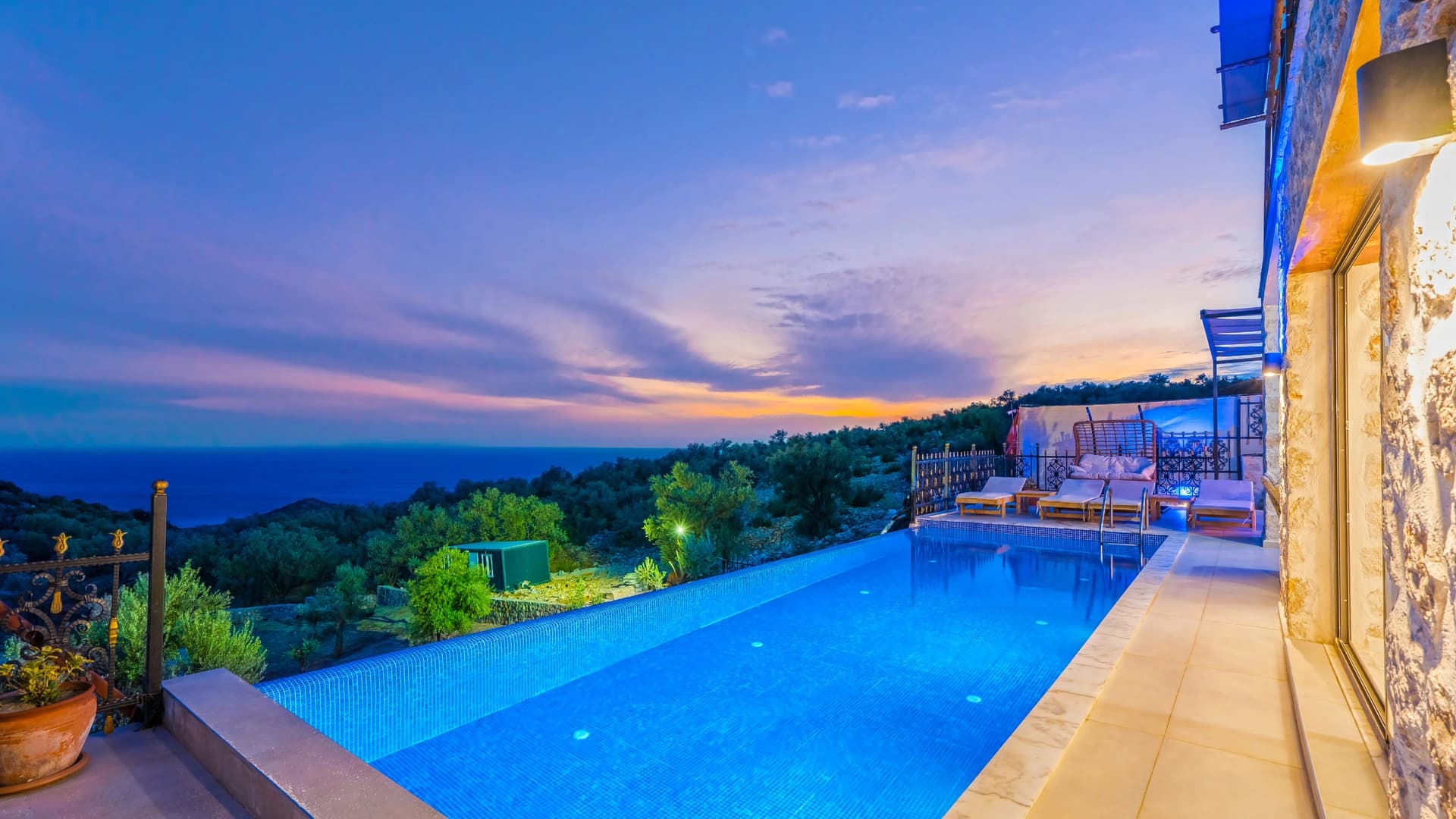 Expansive infinity pool overlooking forested hills and Mediterranean sea at dusk.