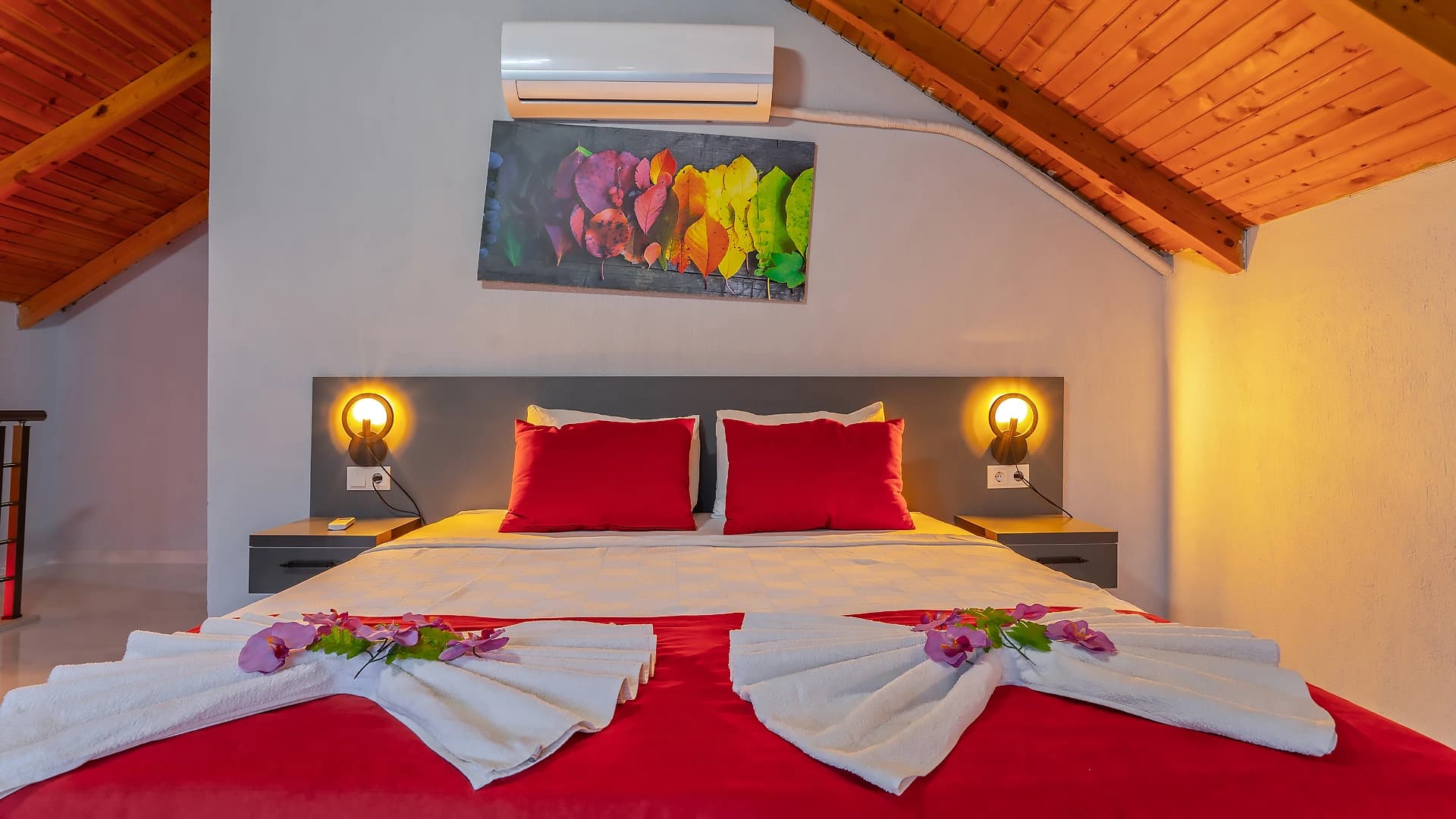 Bedroom with king bed featuring red and white bedding, decorative flowers, and air conditioning unit.