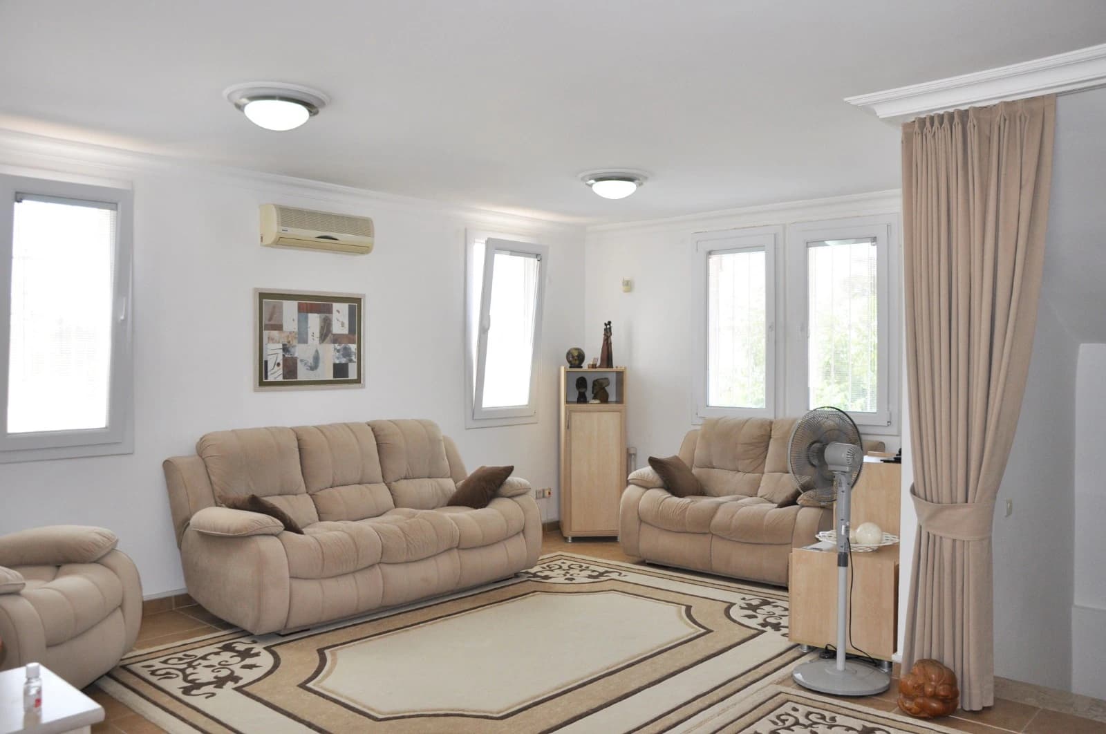 Spacious living room with cream-colored sofas and air conditioning unit.