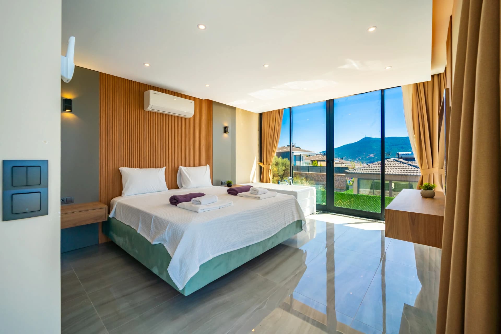 Bright bedroom with king bed and direct balcony access overlooking mountain scenery.