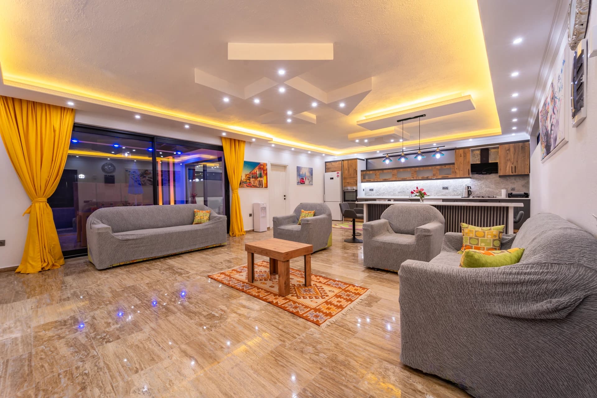 Modern open-plan living room with multiple seating areas, kitchen, and contemporary lighting.