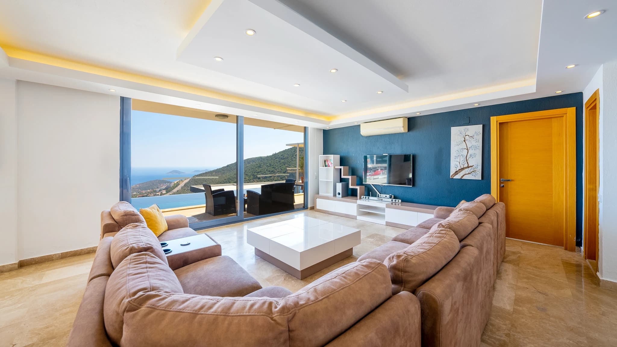 Premium living room with expansive sofa seating, spectacular sea and mountain views through floor-to-ceiling windows, and dark blue feature wall.