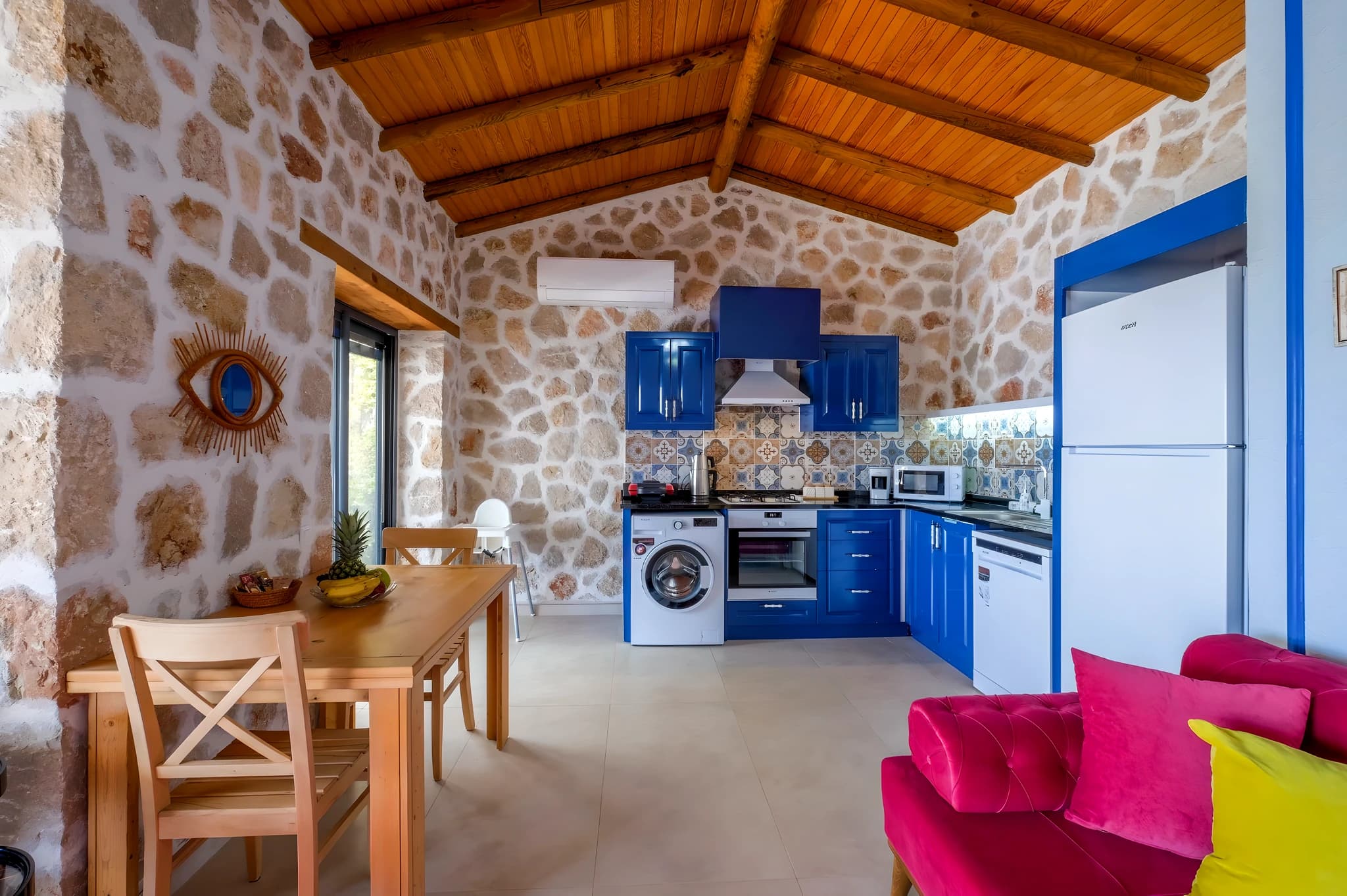 Colorful kitchen with blue cabinetry, integrated appliances, and rustic stone charm.