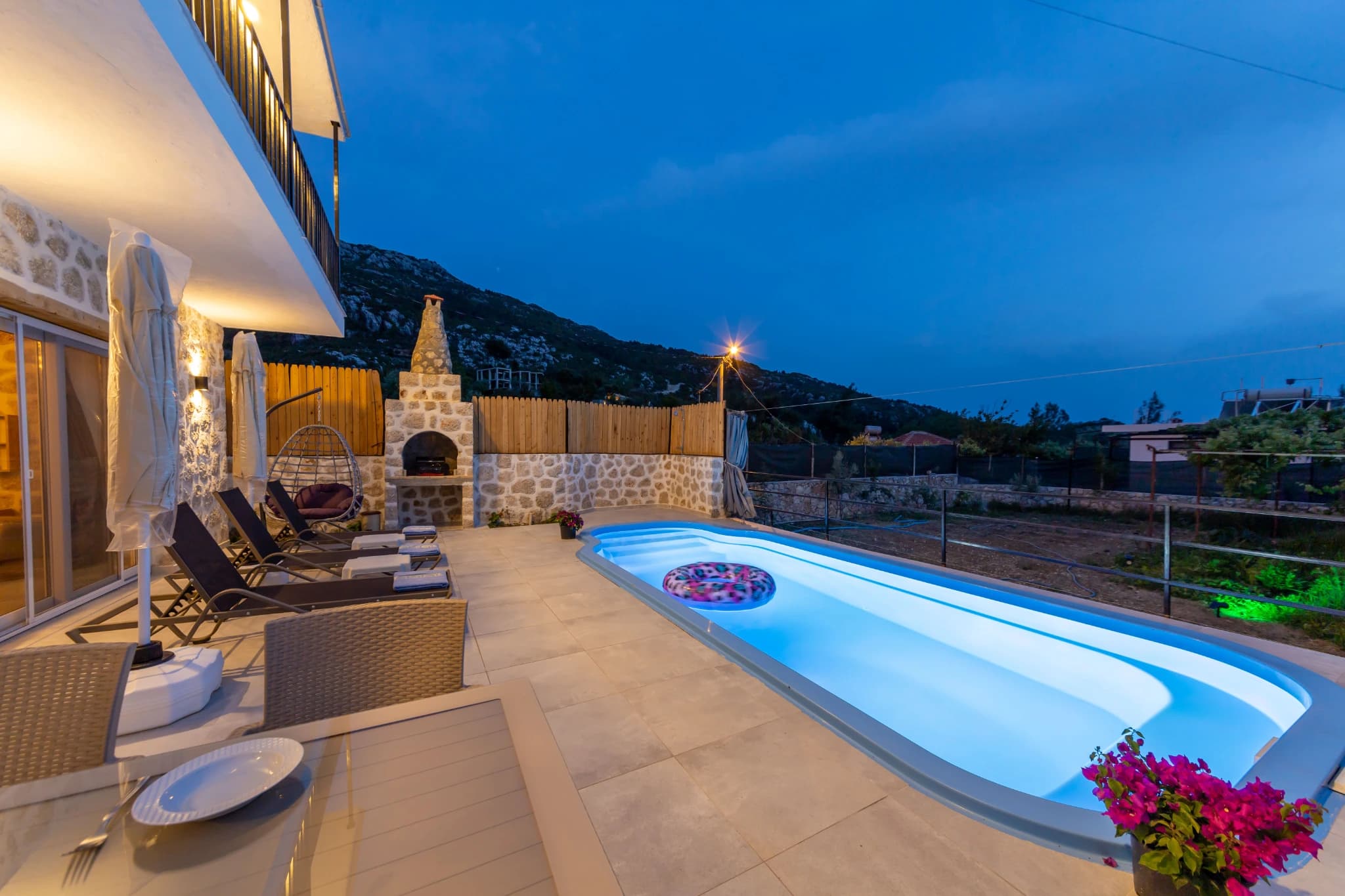 Stunning illuminated private pool at dusk with fireplace and mountain backdrop.