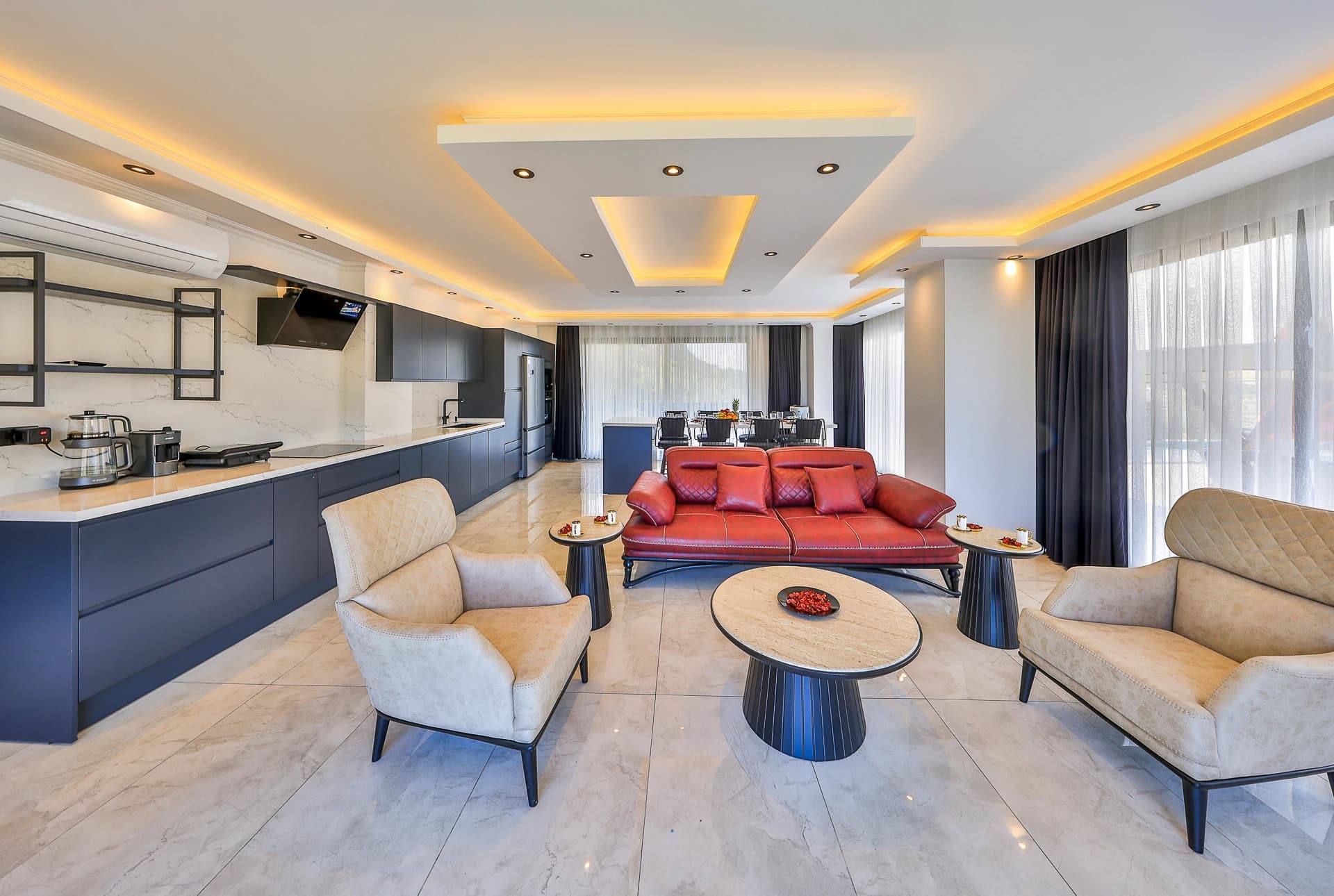 Open-plan living space with red accent sofa, modern armchairs, and integrated kitchen area.