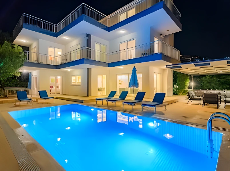 Night-lit pool area with villa illuminated and sun loungers visible.
