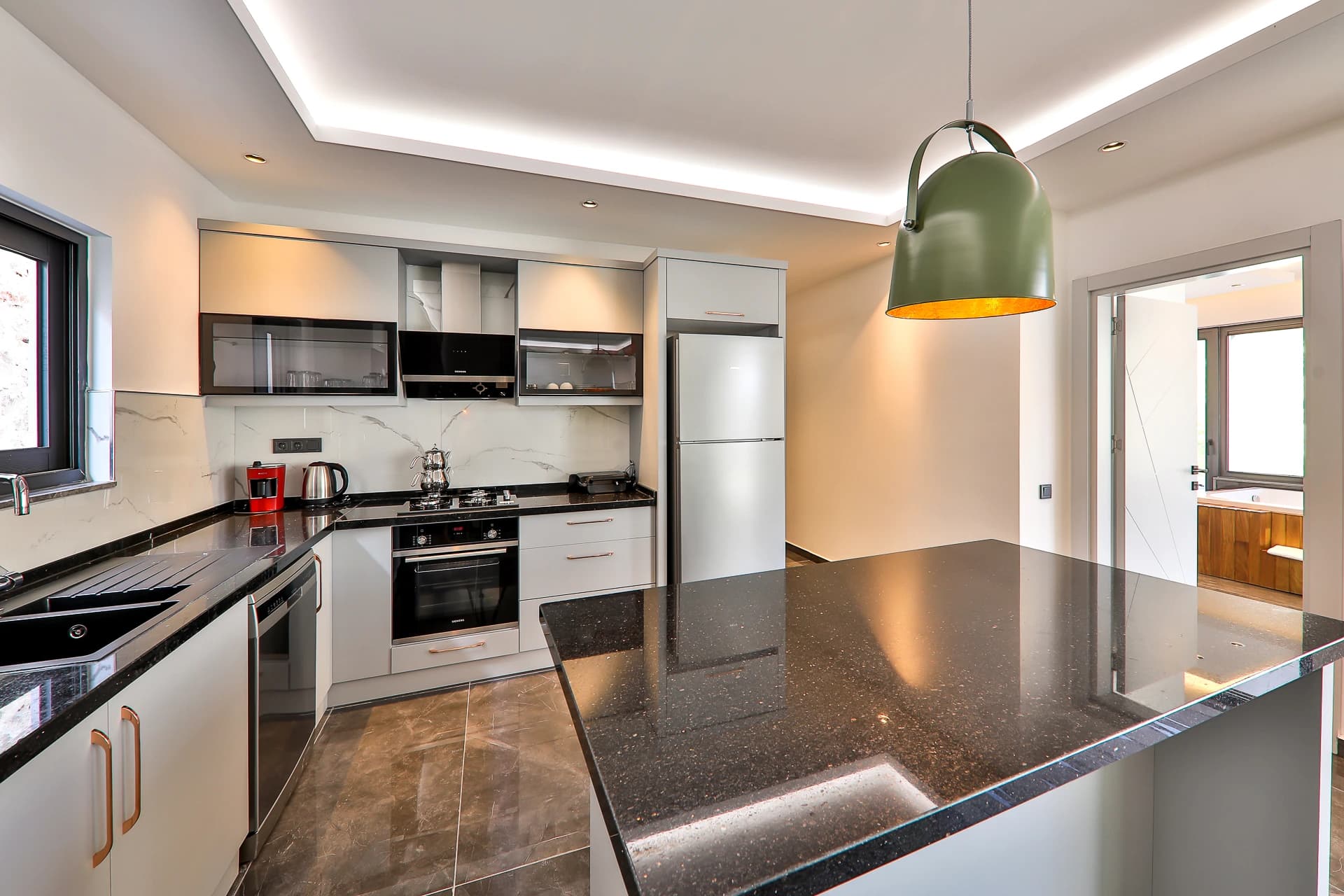 Modern kitchen with white cabinetry, premium appliances, and distinctive green pendant lighting.