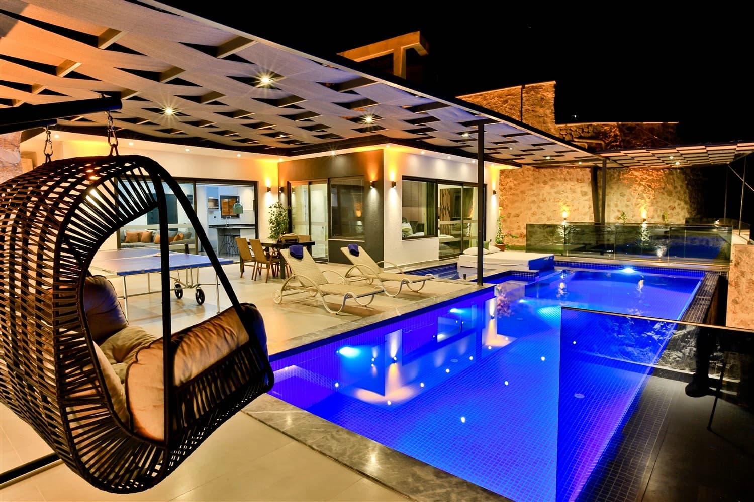 Stunning illuminated private pool at night with lounge seating and pergola-covered terrace.