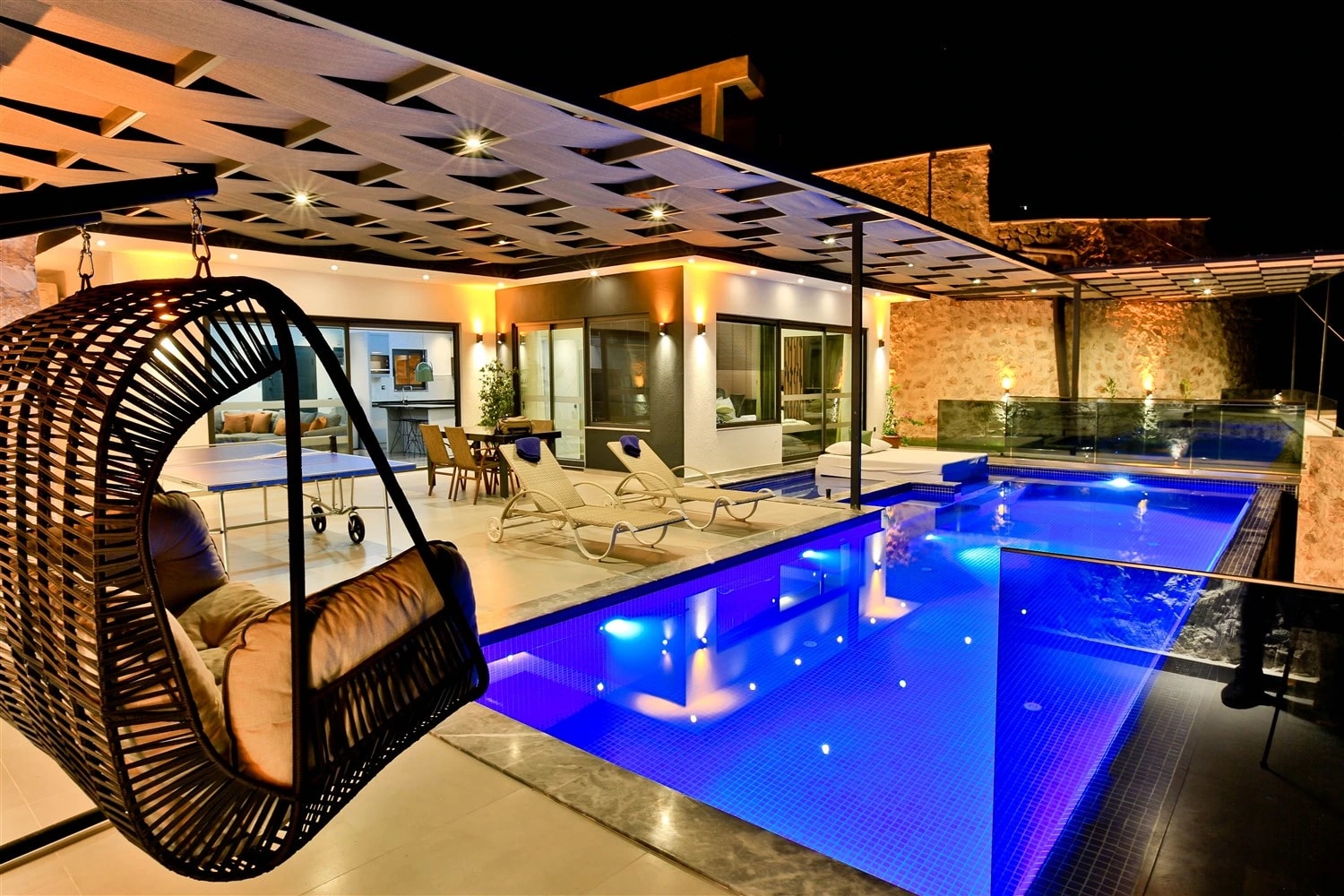 Stunning illuminated private pool at night with lounge seating and pergola-covered terrace.
