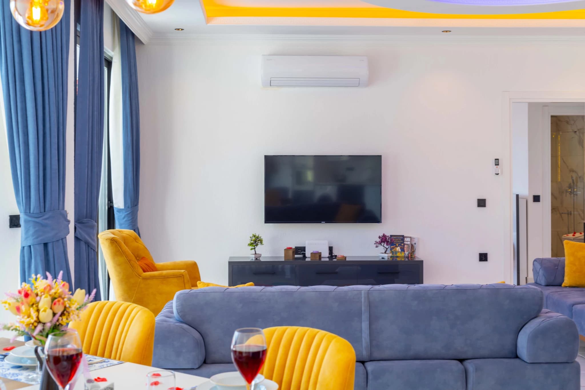 Kalkan'da Doğa Manzaralı, Özel Havuzlu ve Korunaklı Bahçeli Villa – Spacious living area with comfortable seating, entertainment system, and elegant yellow and blue color scheme.