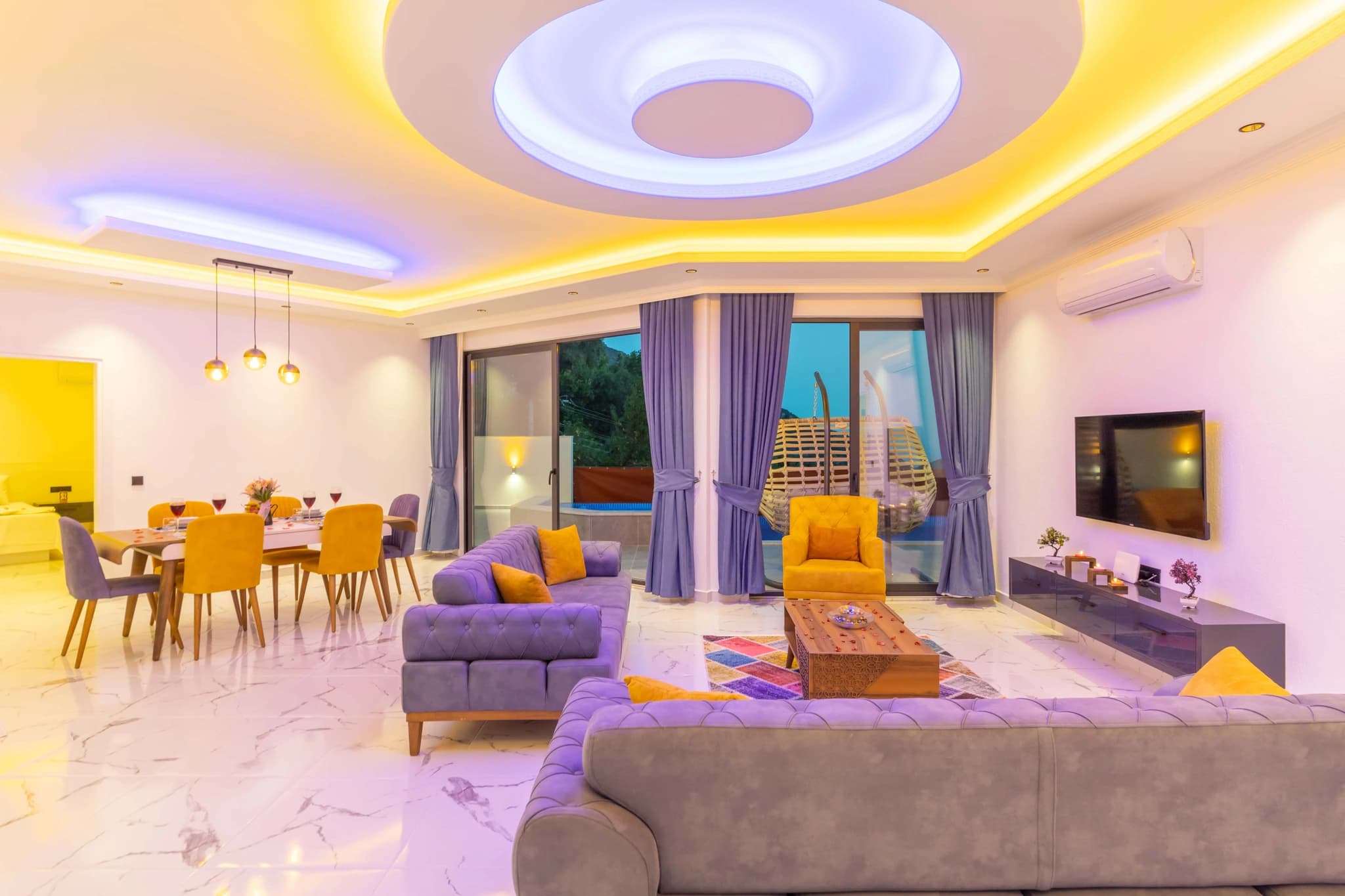 Kalkan'da Doğa Manzaralı, Özel Havuzlu ve Korunaklı Bahçeli Villa – Open-plan living room with modern purple sofas, accent lighting, and nature views terrace access.