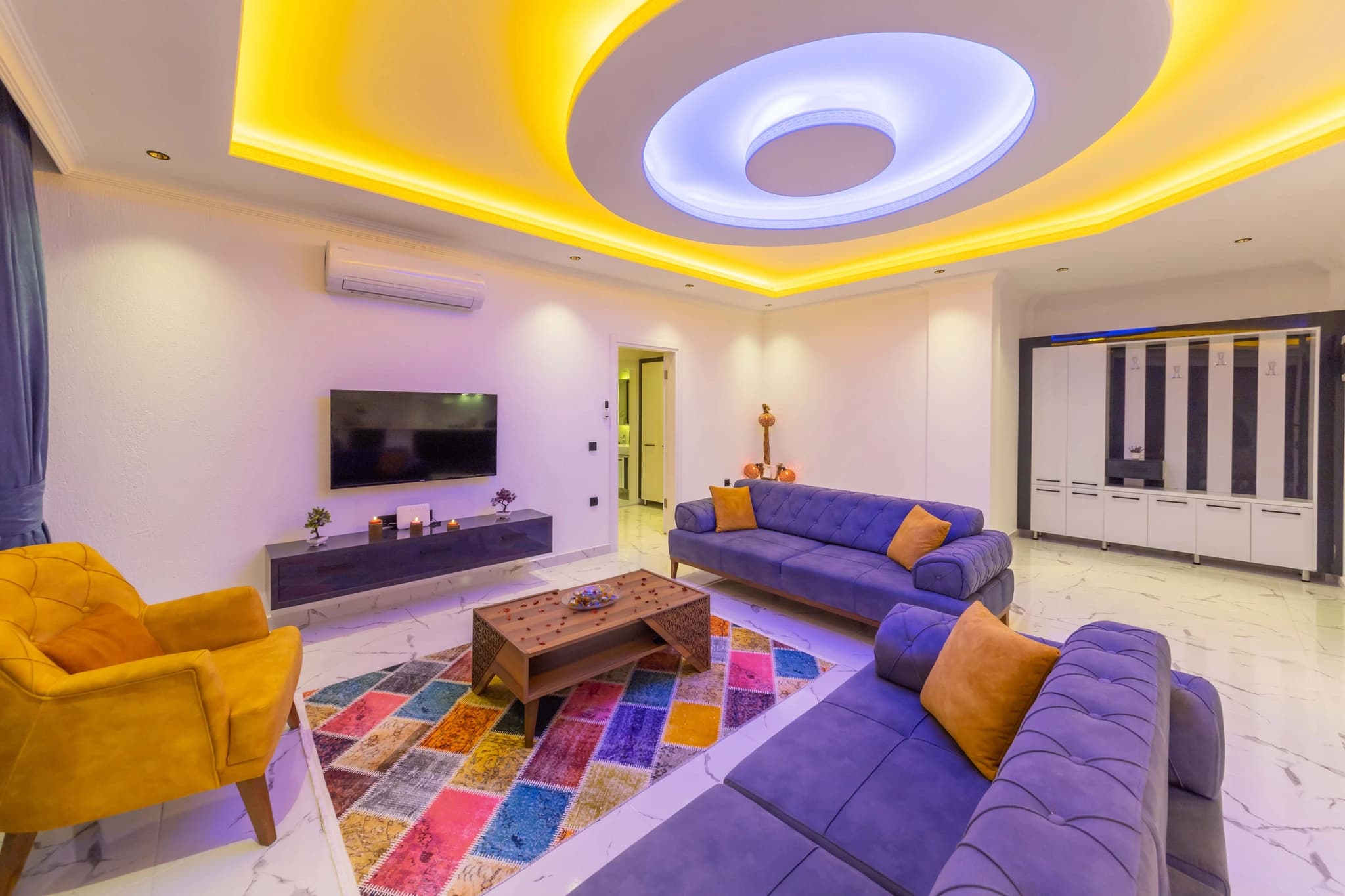 Kalkan'da Doğa Manzaralı, Özel Havuzlu ve Korunaklı Bahçeli Villa – Spacious living room with purple and yellow seating, LED accent ceiling, and contemporary décor.