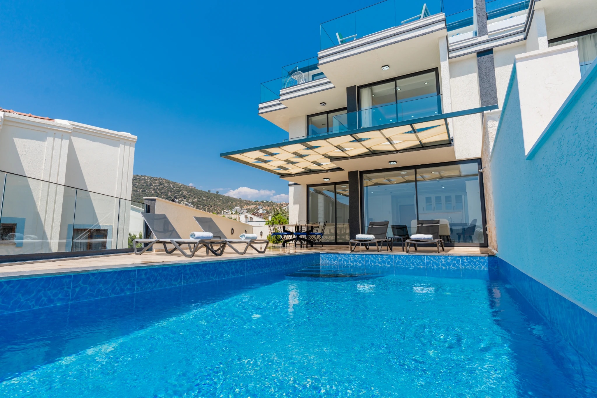 Crystalline pool with modern villa facade and mountain scenery in the background.