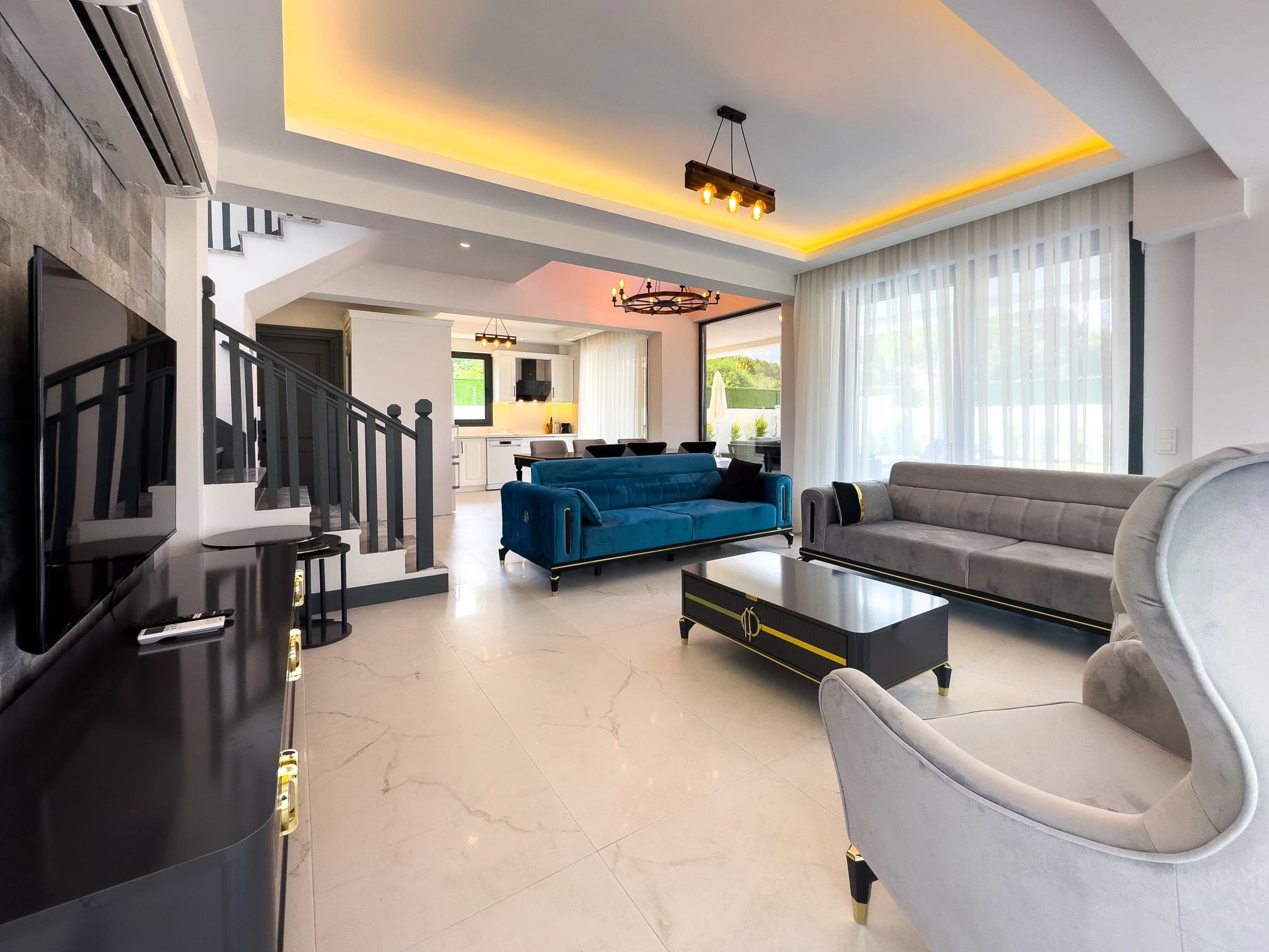 Open-plan living area with blue and gray upholstered seating, elegant coffee table, and access to dining area.