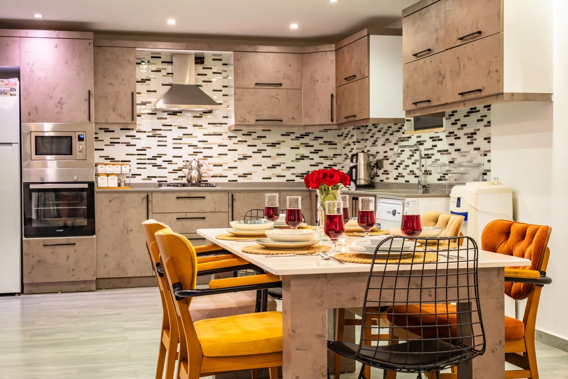 Modern kitchen with island dining, tiled backsplash, and integrated appliances.