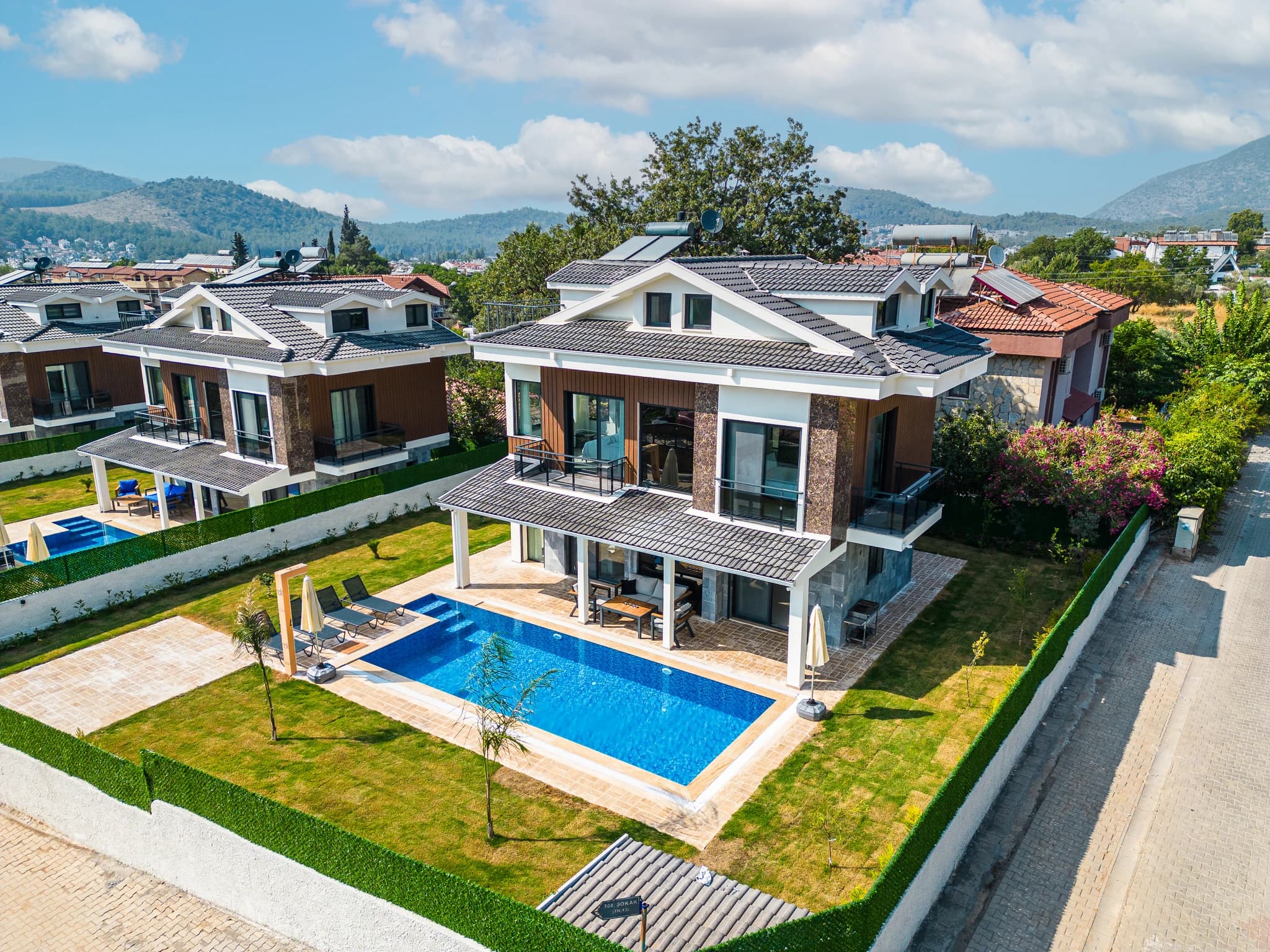 Close aerial view of villa with private pool, covered terrace, and manicured garden with mountain backdrop.