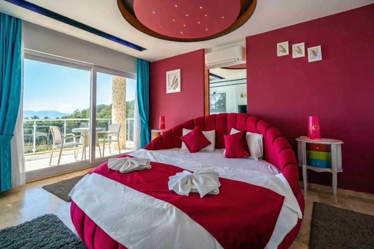 Luxurious master bedroom with striking red velvet headboard and panoramic sea and mountain views.