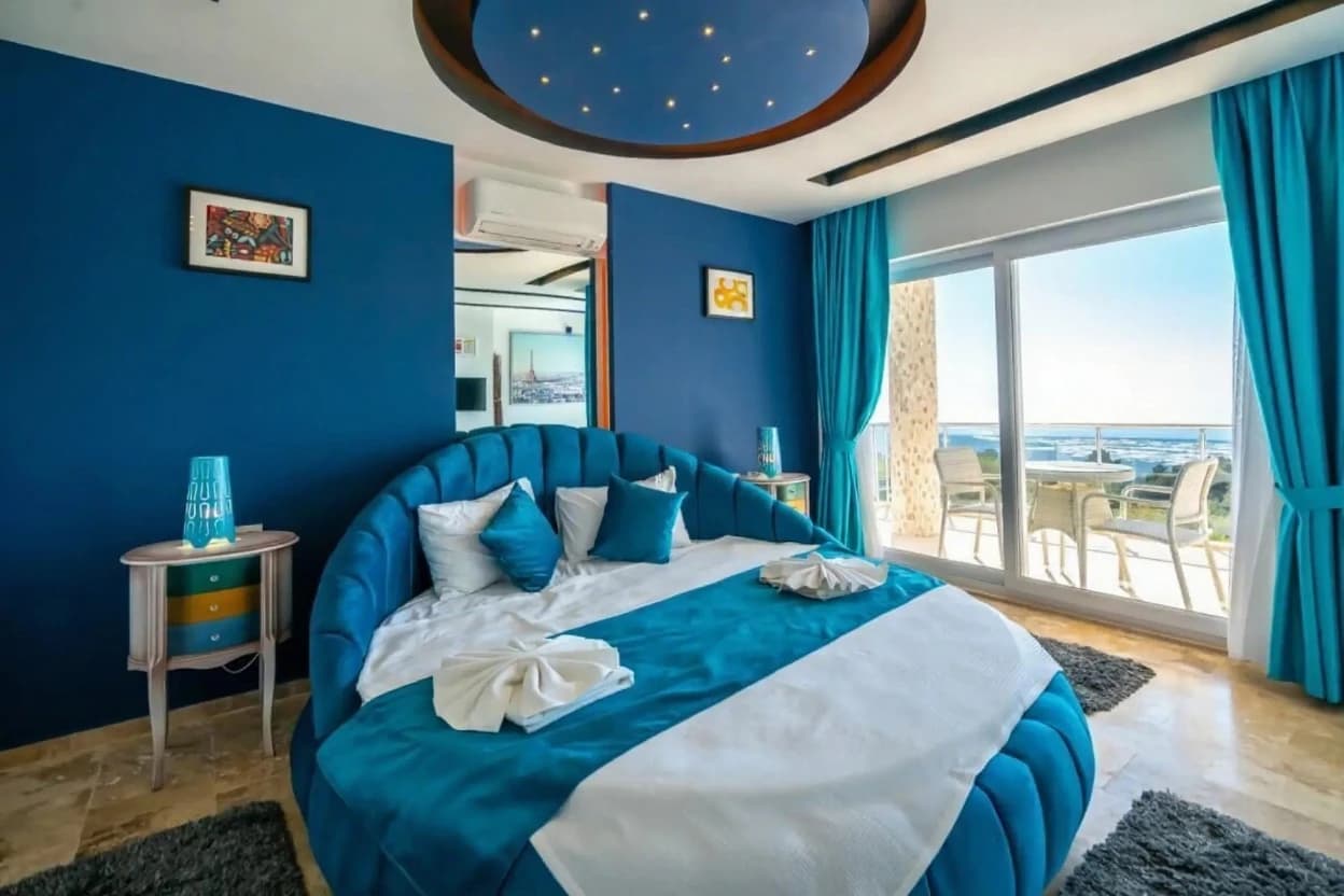 Elegant blue bedroom featuring a distinctive round bed with ocean and mountain vistas.