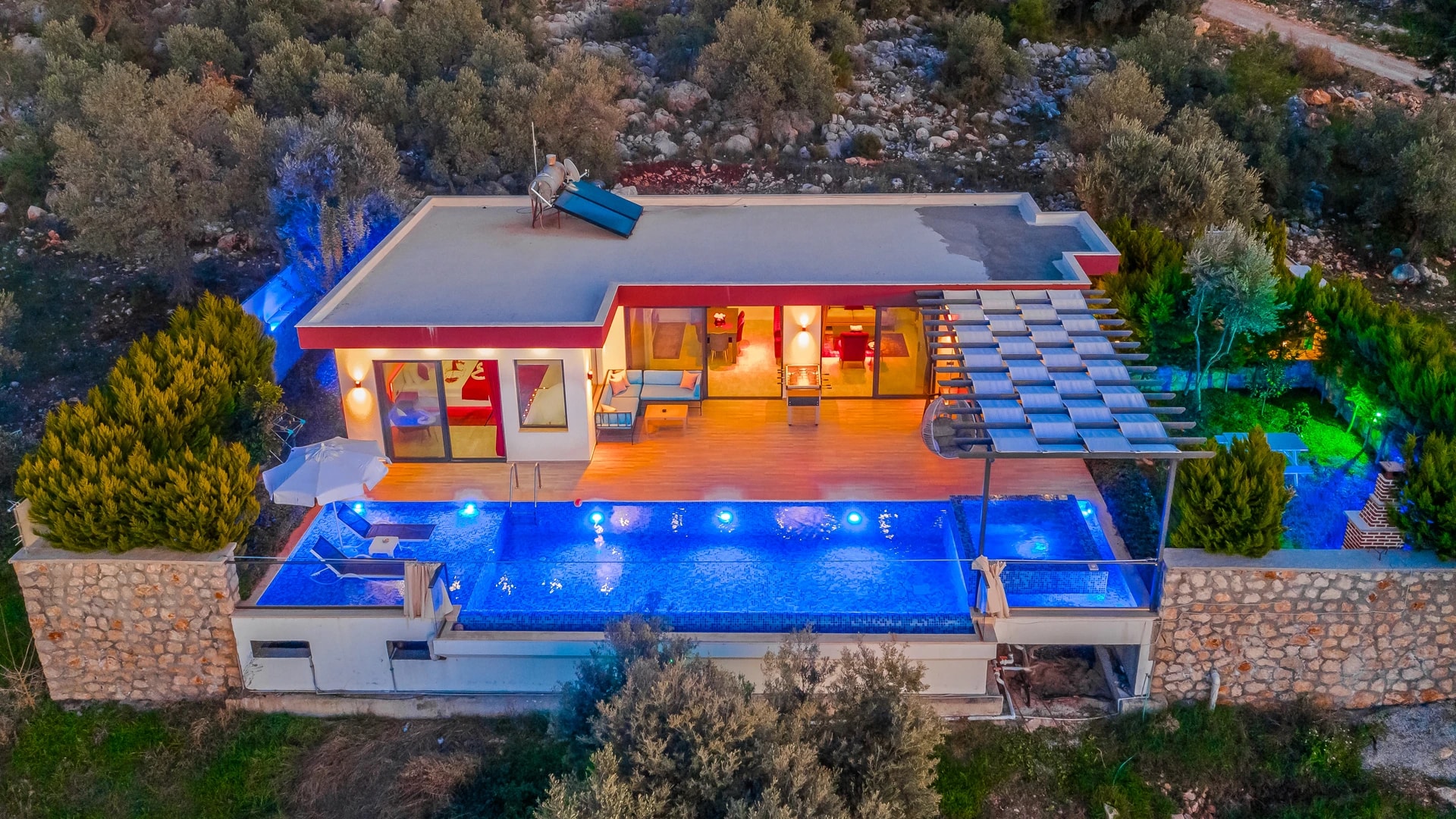 Stunning aerial view of glowing blue pool with modern villa and mountainous surroundings.