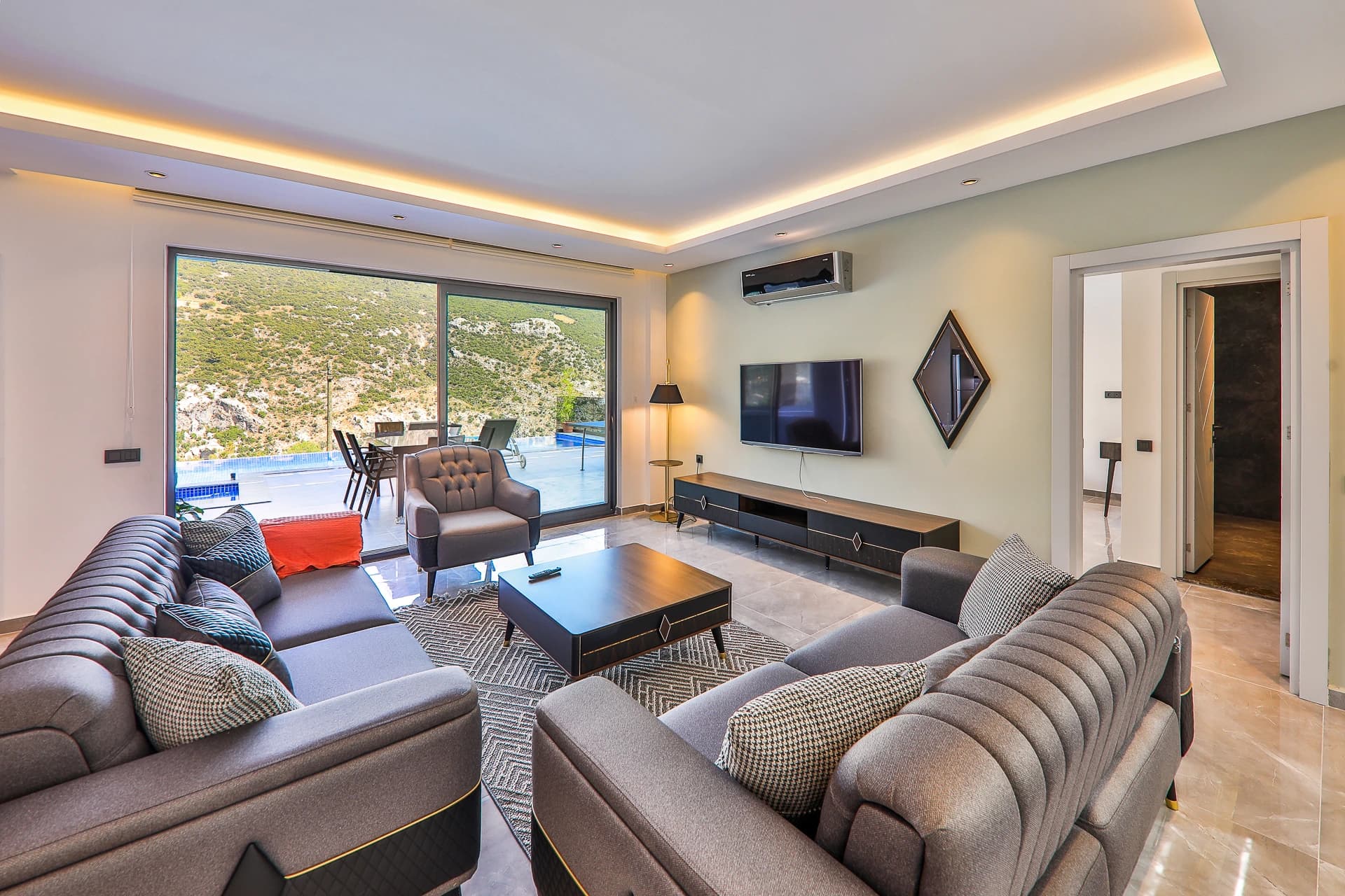 Spacious living room with sofas, smart TV, and panoramic views to pool and mountains.