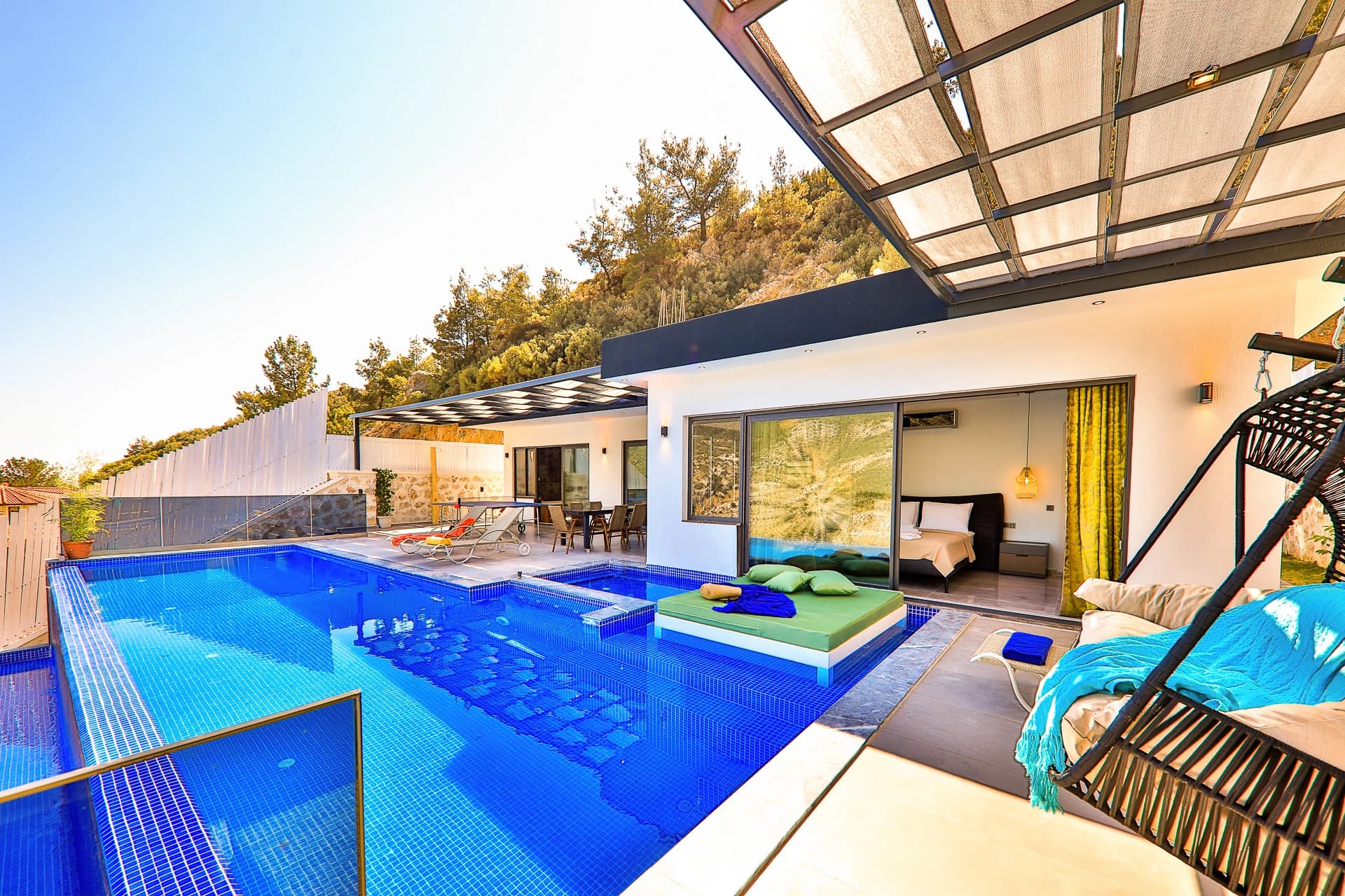 Resort-style pool terrace with multiple lounging areas, hanging seating, and direct bedroom access with scenic views.