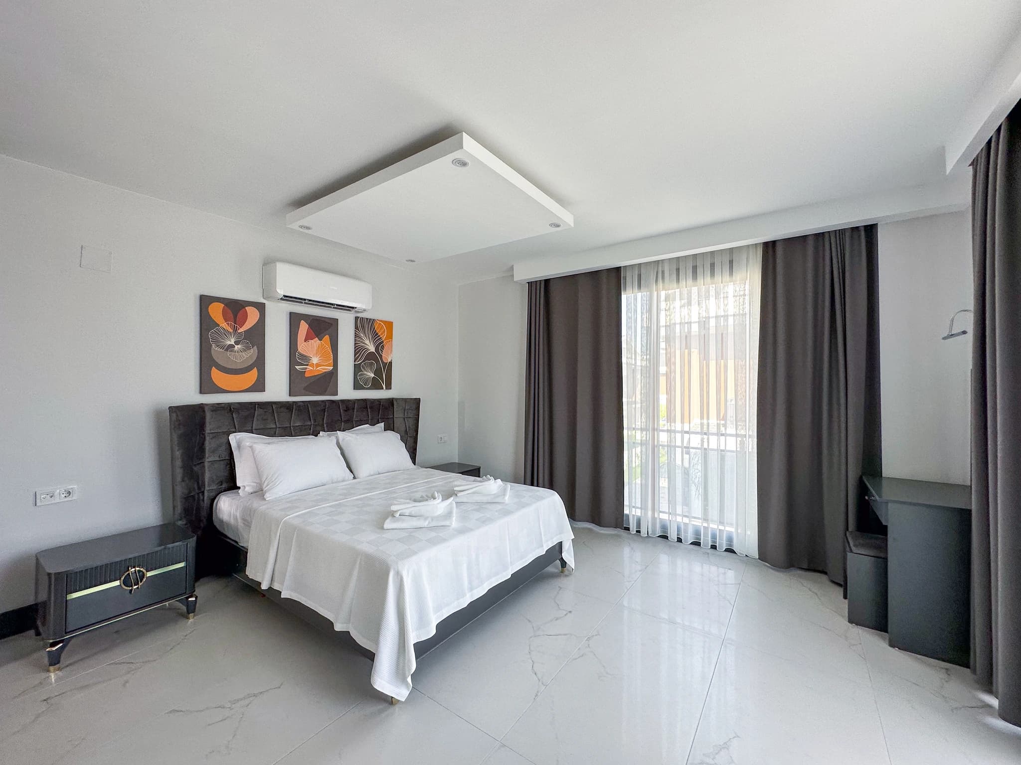 Spacious master bedroom with king bed, air conditioning unit, and access to a balcony with garden views.
