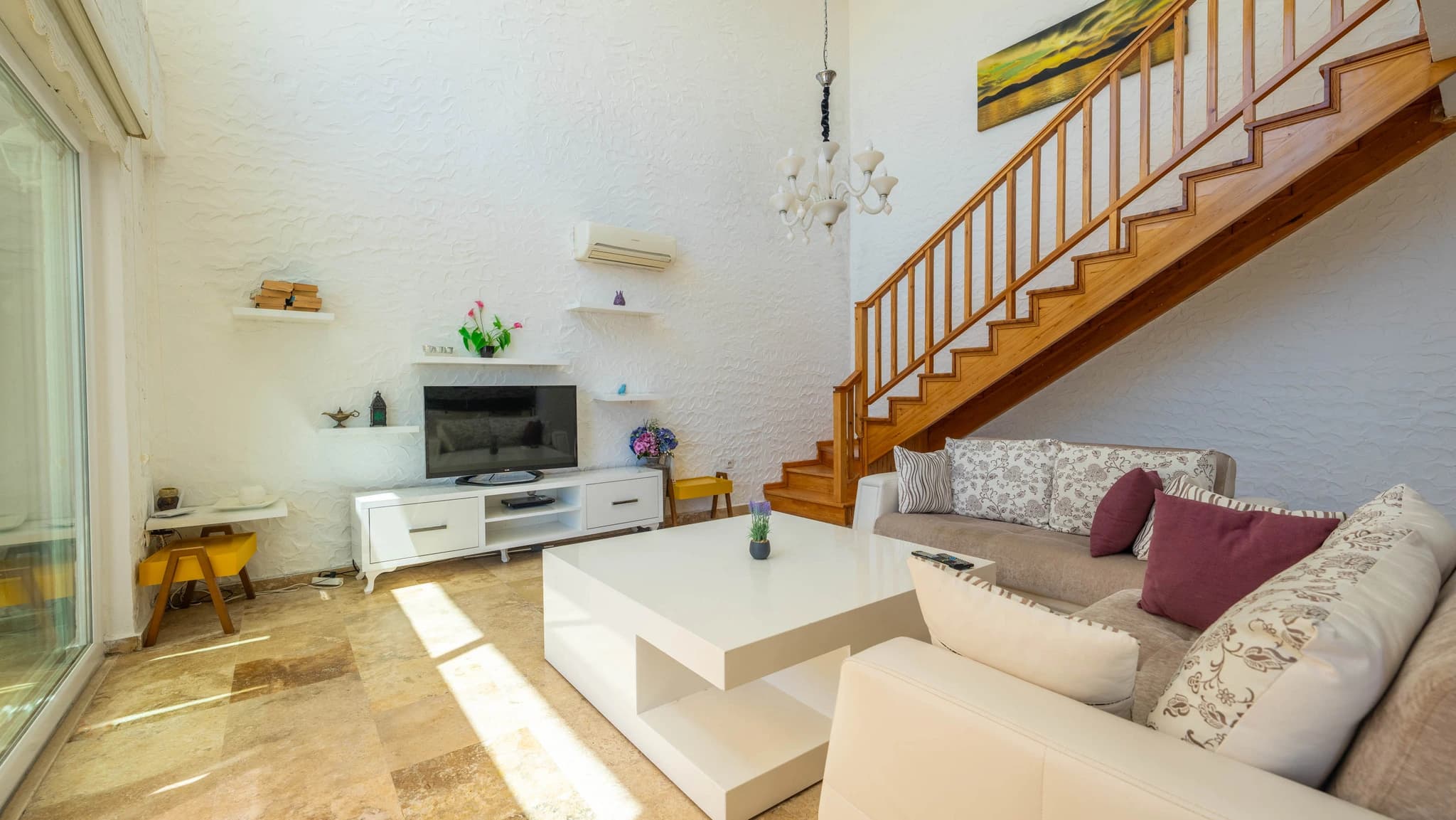 Open-plan living room with modern sofa, TV unit, wooden staircase, and bright natural lighting.